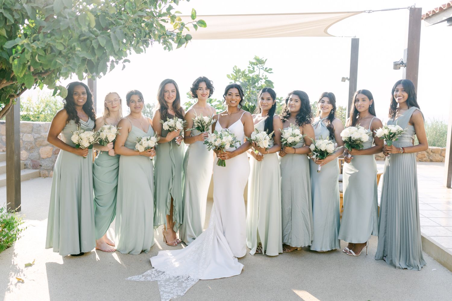 Wedding party poses with bouquets of white flowers wearing sage green bridesmaid dresses.