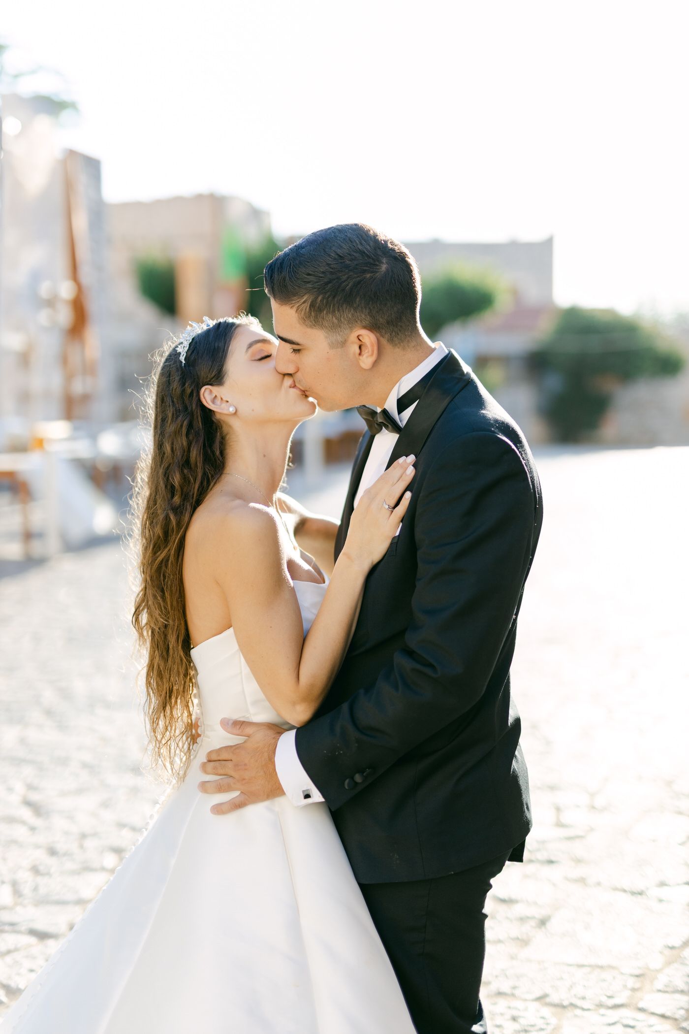Romantic couple sharing a wedding day kiss on a sunny beach with long white gown and black tuxedo.