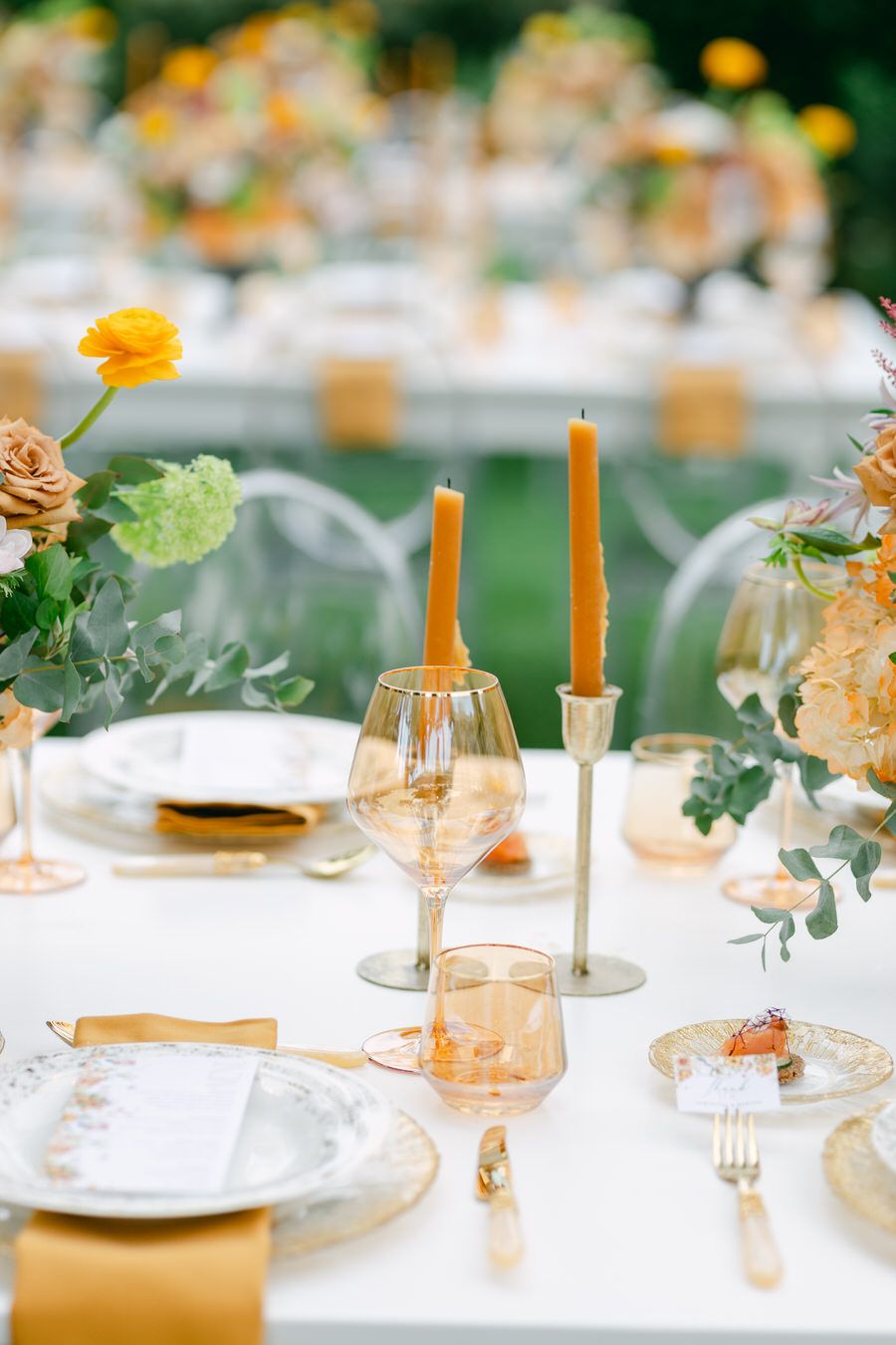 Wedding table setting with orange candles, glassware and floral centerpieces.