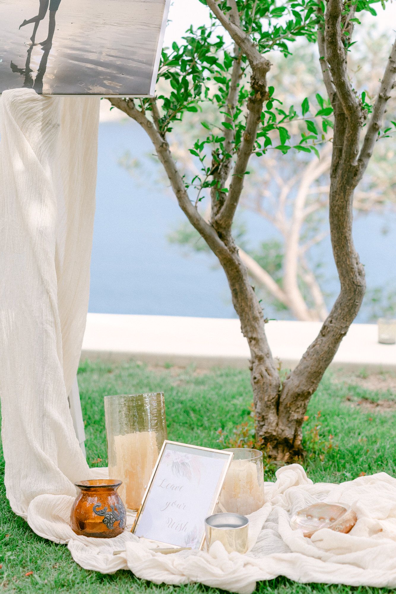 Romantic outdoor picnic setup with white linens and champagne under a small tree.