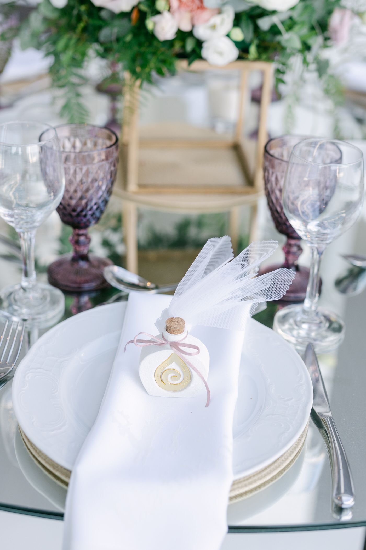 Elegant table setting with purple wine glasses, white napkin, and decorative feather detail on mirrored surface.