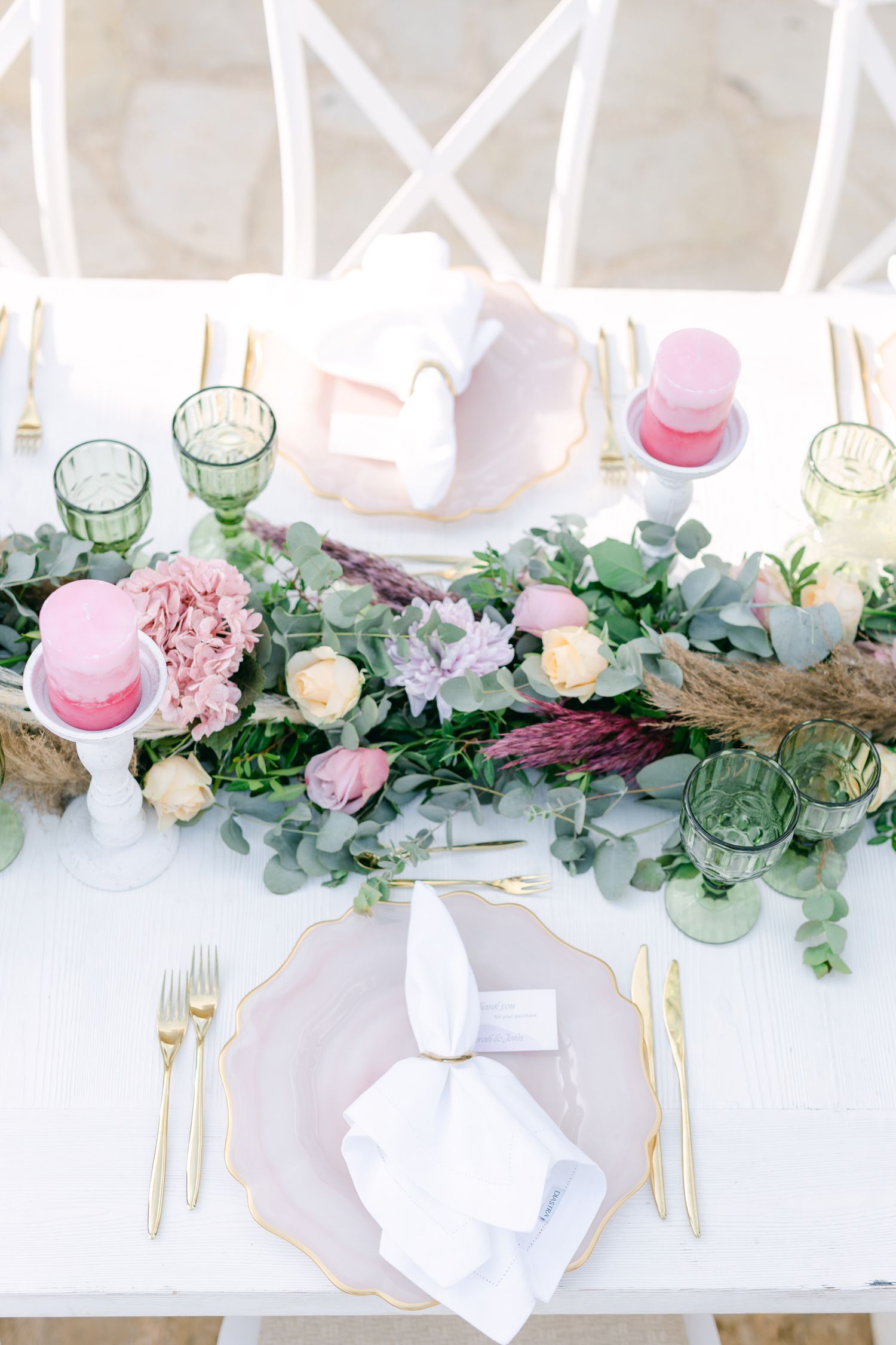 Elegant table setting with pink and green floral runner, vintage glassware, and gold cutlery.