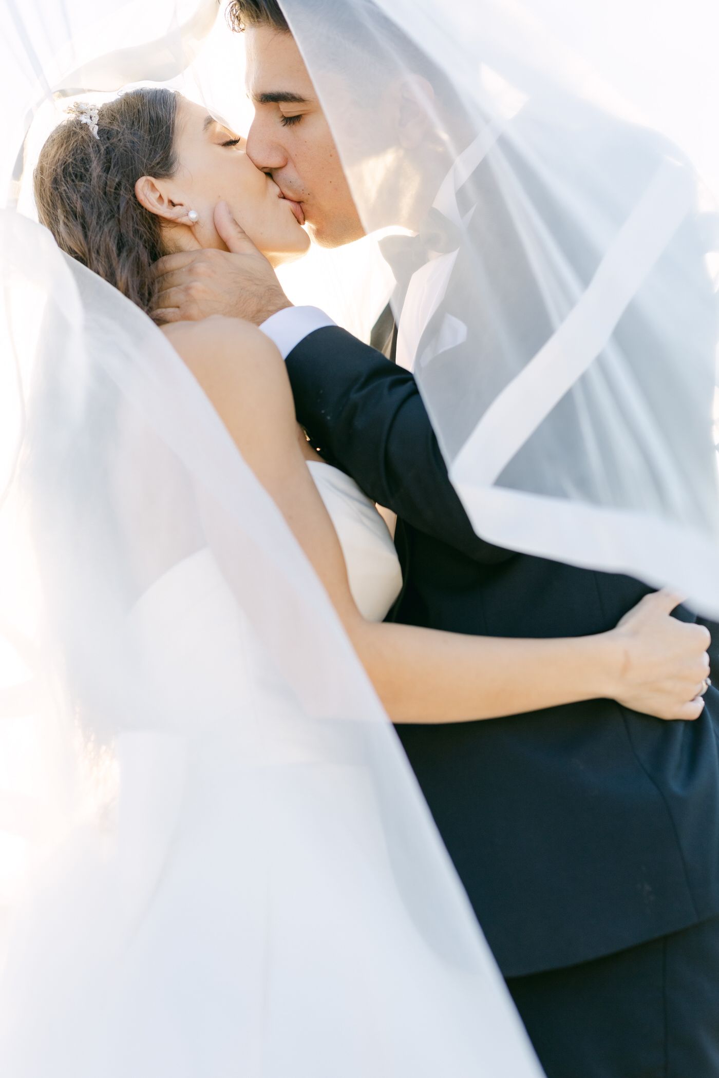A romantic wedding kiss captured under a flowing veil with soft lighting.