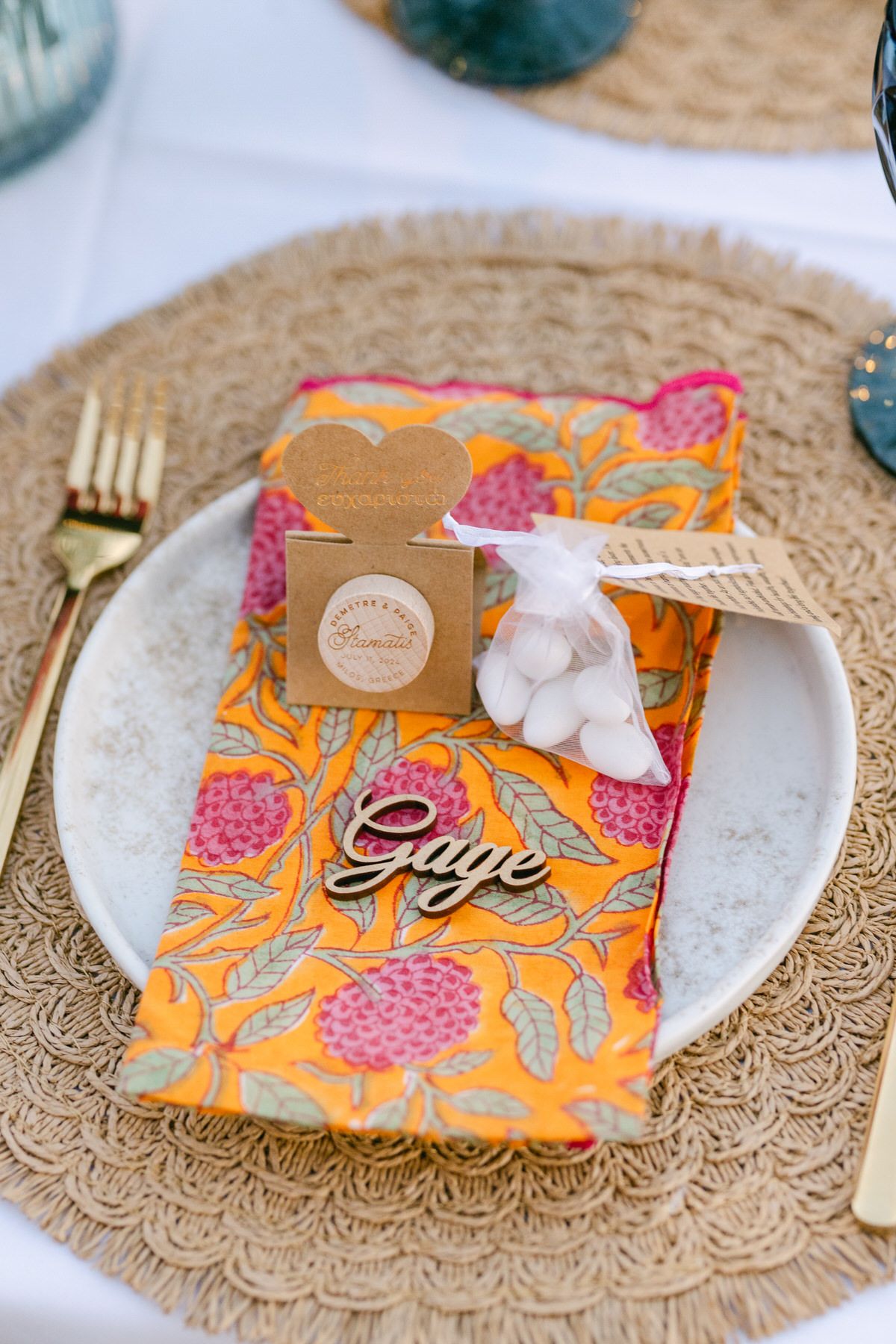 Place setting with orange floral napkin, gold charger plate, gift box and decorative elements at a formal event.