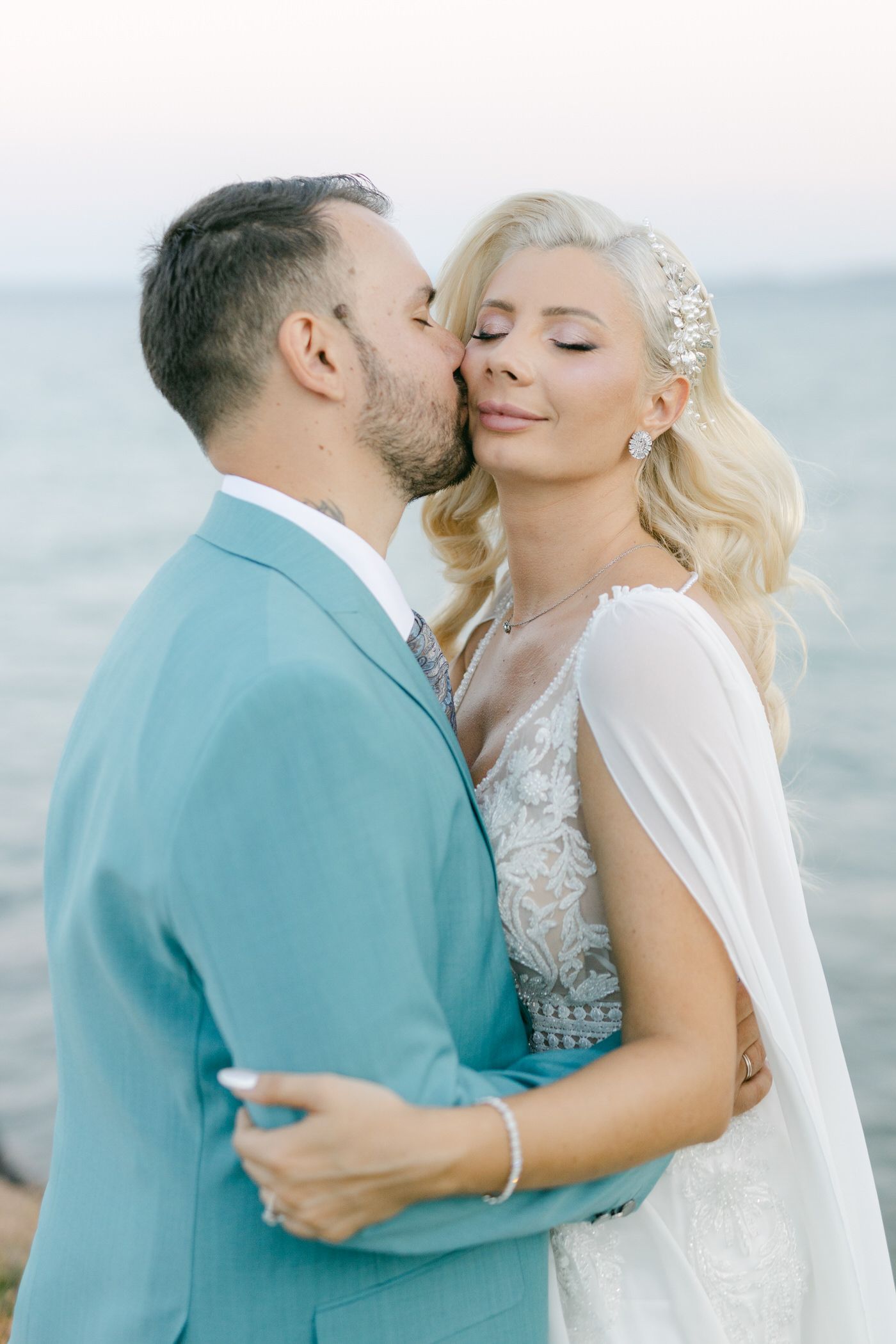 A romantic beach wedding moment between a couple in a turquoise suit and white lace gown by the ocean.