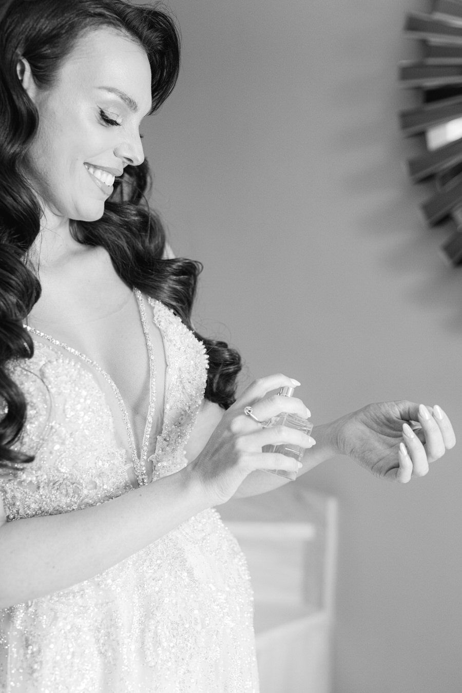 Elegant bride in lace dress spraying perfume with playful smile.