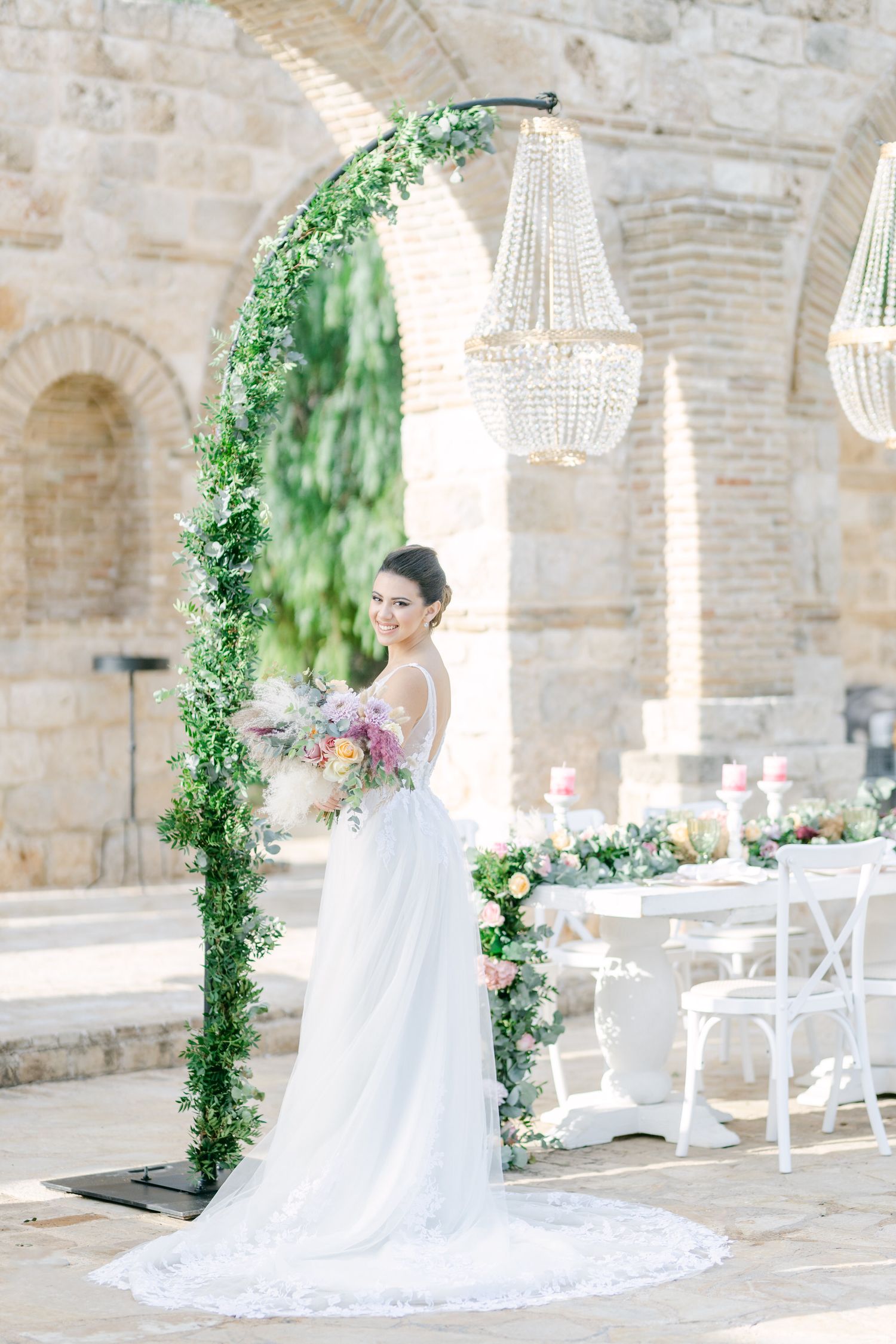 Elegant wedding setup with a greenery arch, crystal chandeliers, and stone architecture.