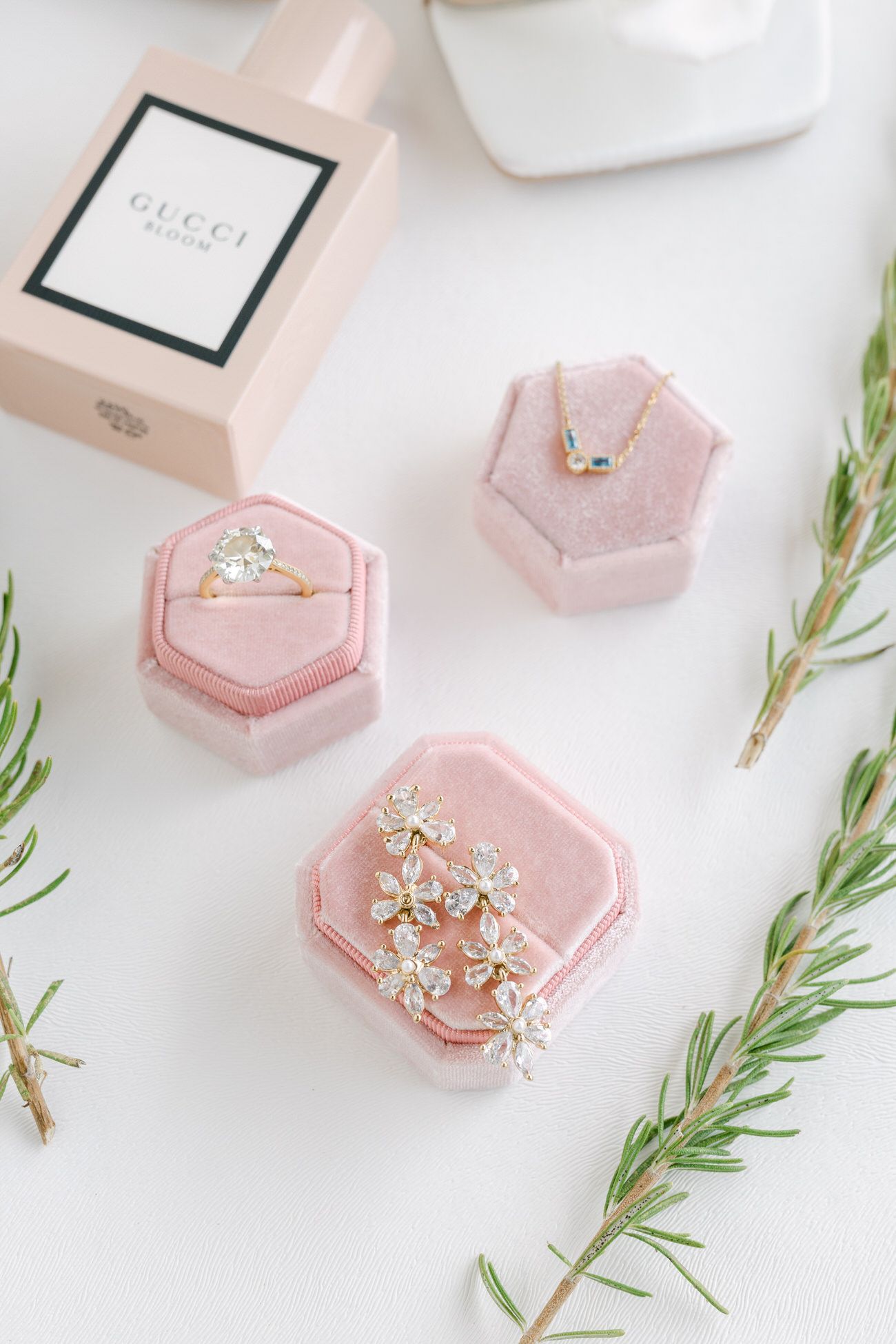 Pink jewelry boxes with rings and Gucci perfume bottle arranged with sprigs of rosemary.