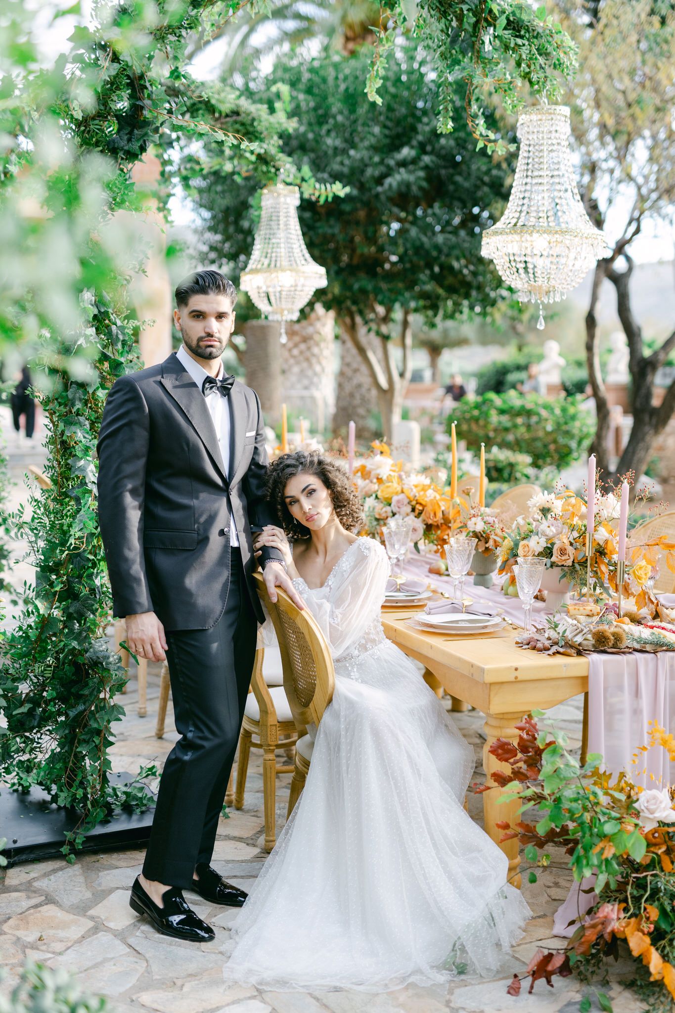 Elegant outdoor wedding reception setup with crystal chandeliers and autumn floral arrangements on a rustic wooden table.