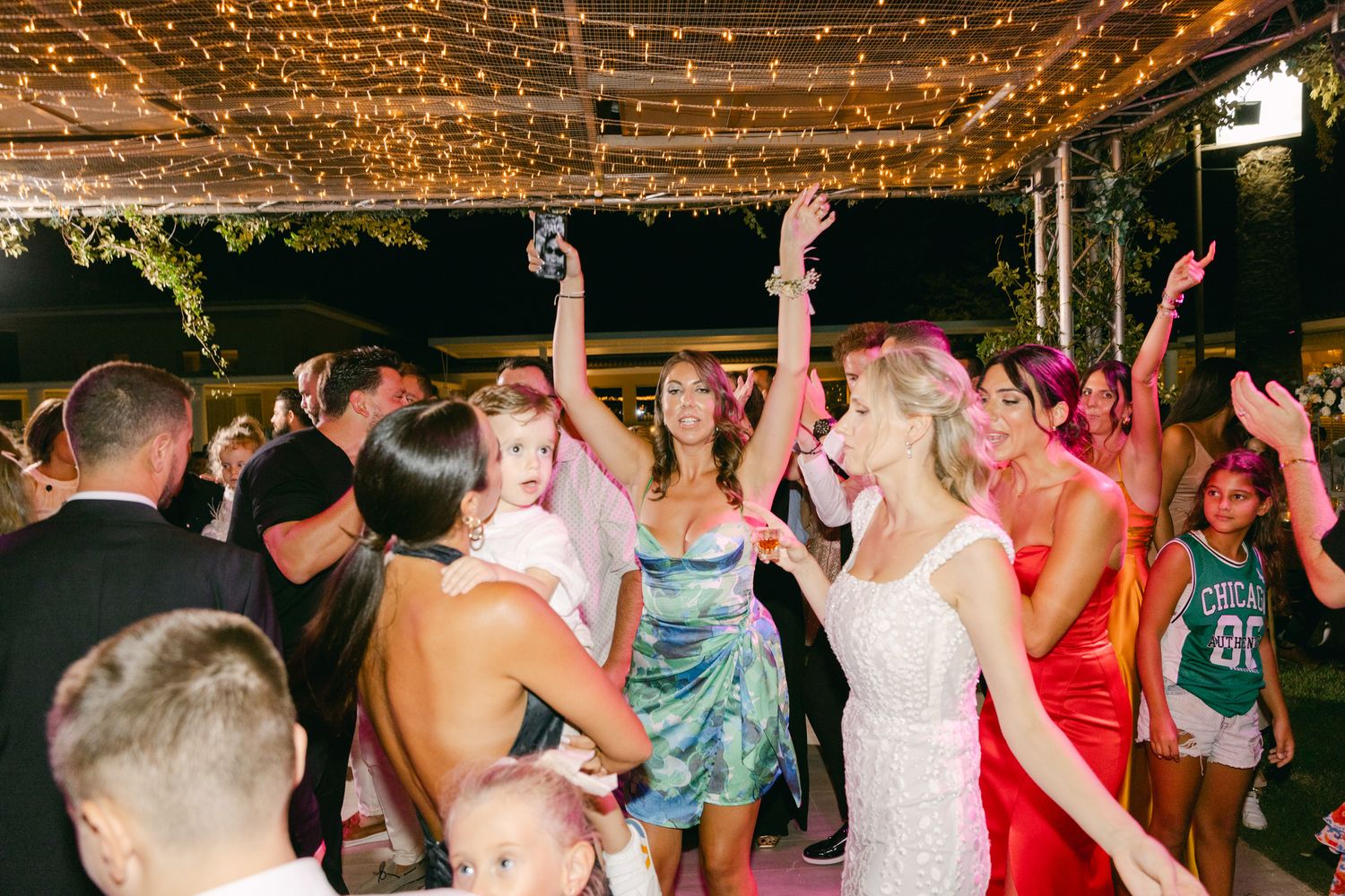 Wedding reception dance floor filled with energetic guests under twinkling lights during evening celebration.