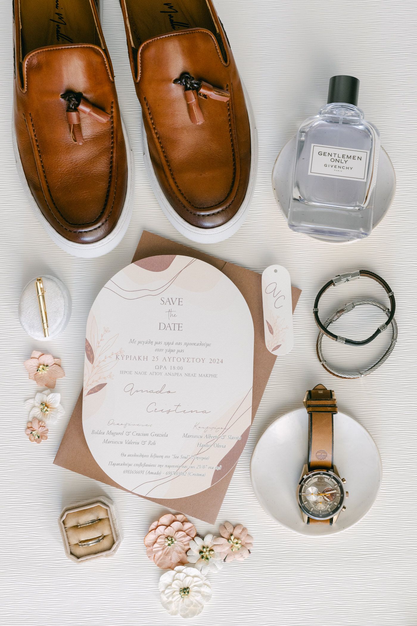 Wedding day accessories flatlay with brown leather shoes, cologne, invitation, watch and rings on white background.