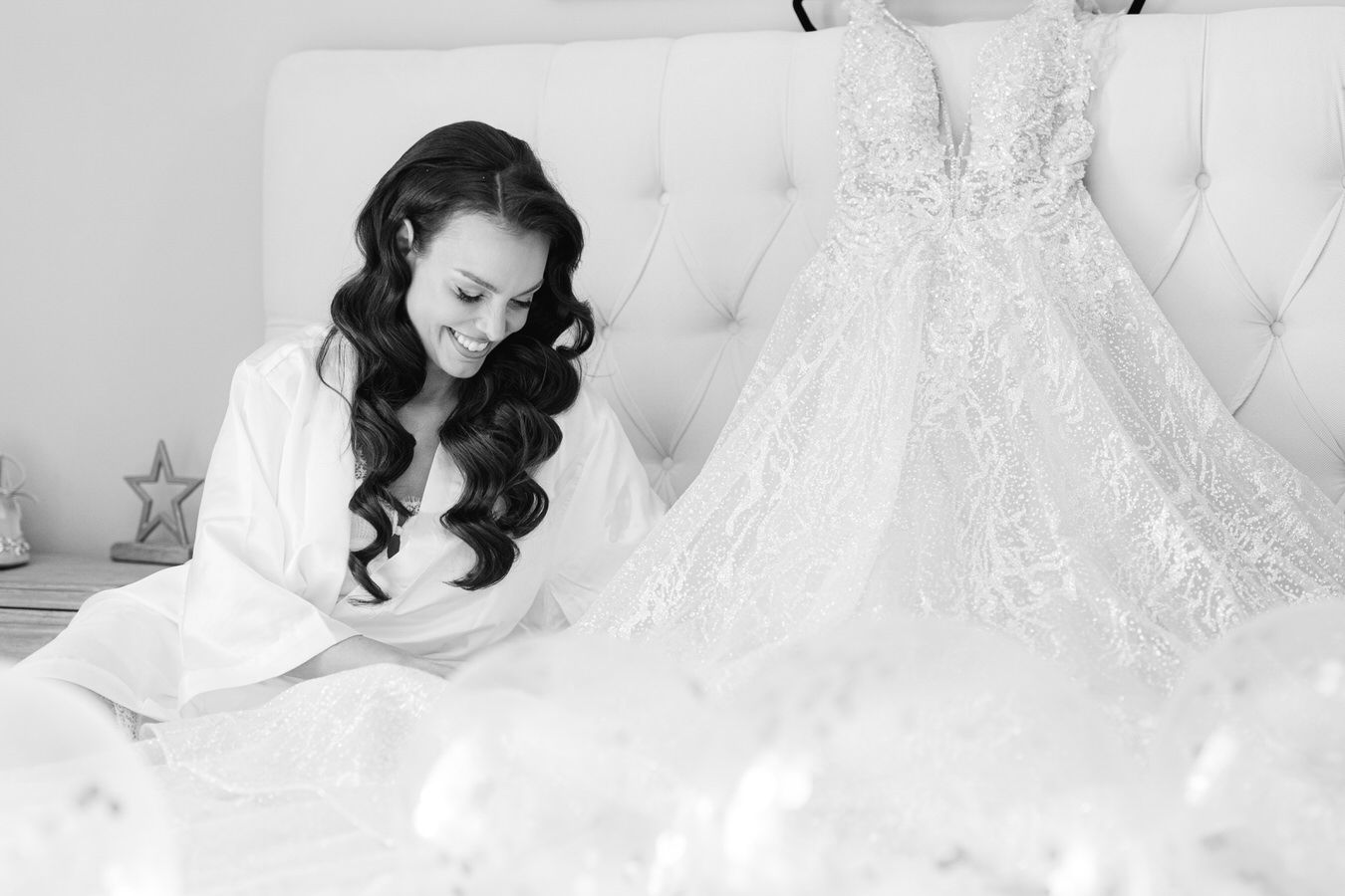Black and white portrait of bride admiring wedding gown before ceremony.