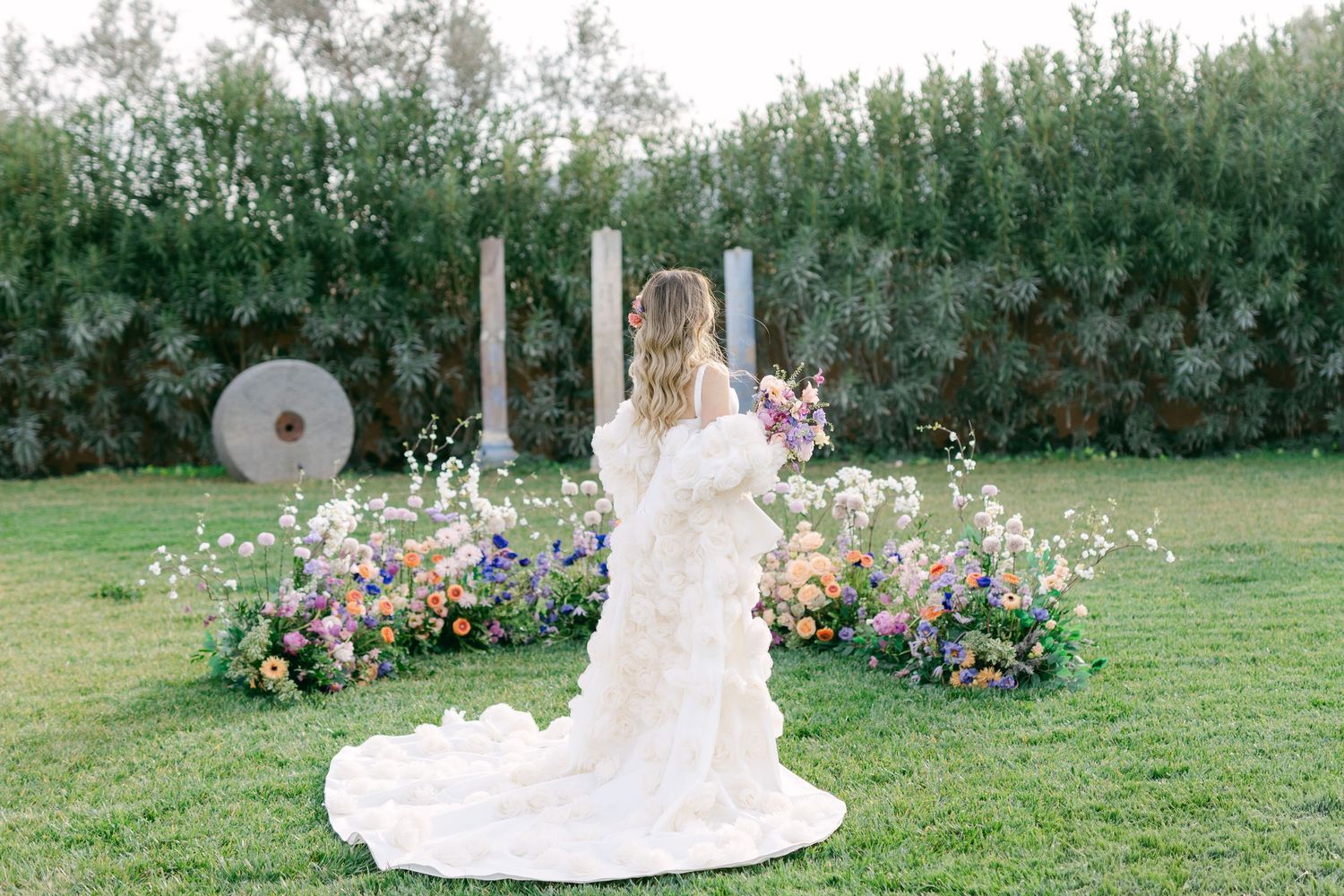 Beautiful outdoor wedding scene with floral arch and colorful flower arrangements on a lush green lawn.