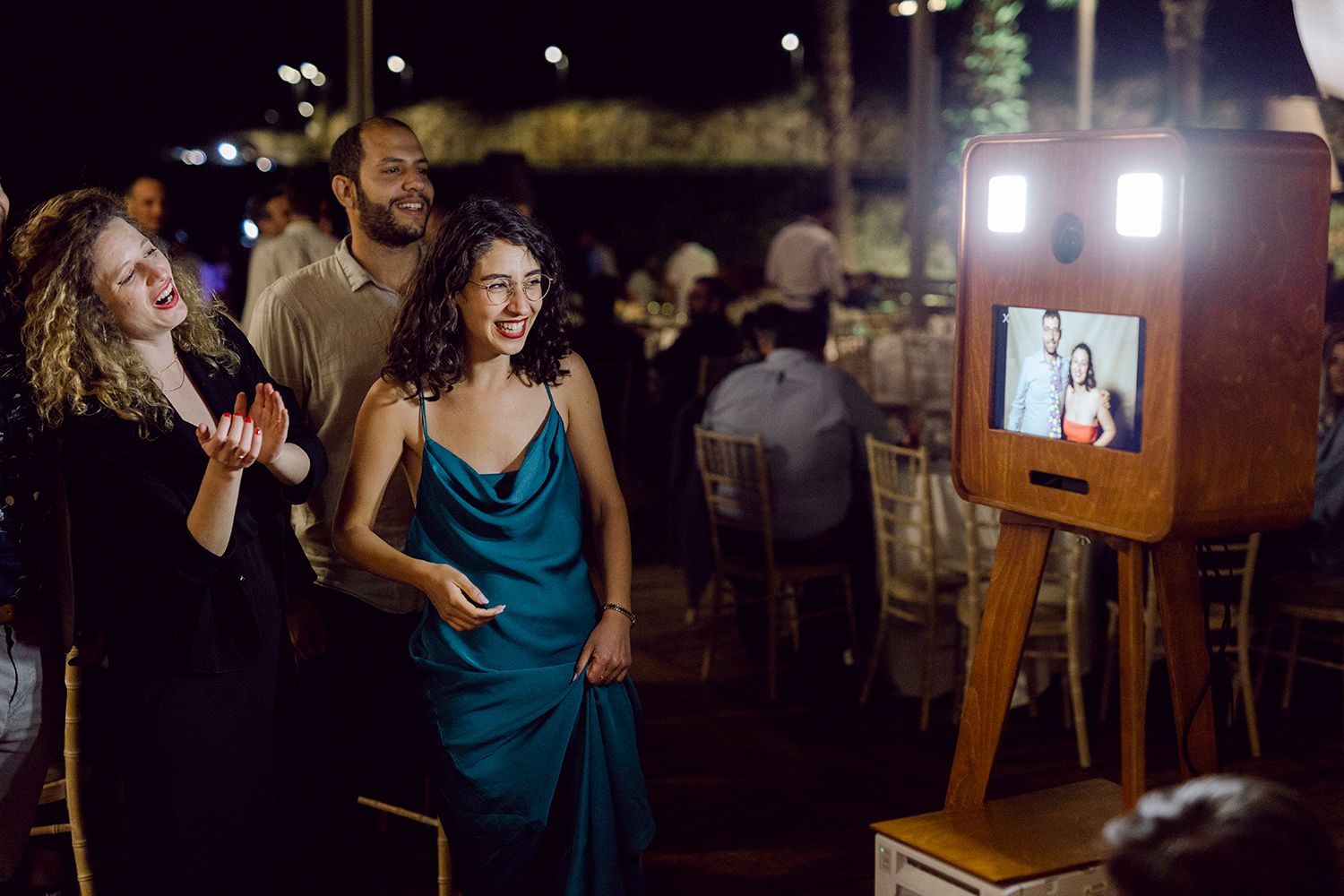 People react with excitement while watching a display screen at a nighttime outdoor event and celebration.