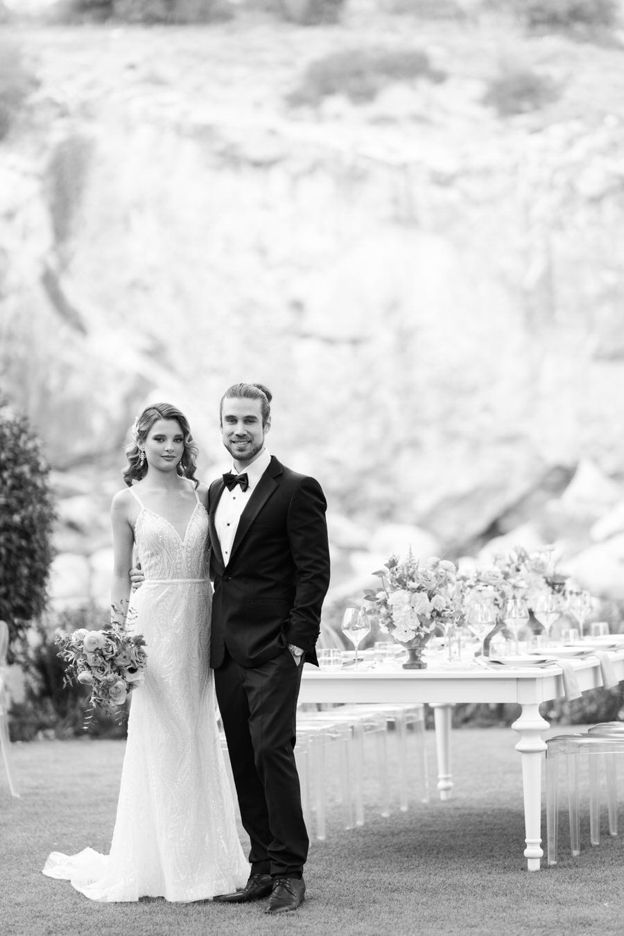 A black and white portrait of a couple by an elegant white reception table.