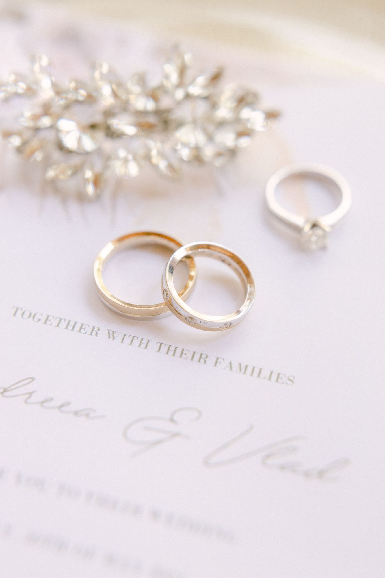 Wedding rings and crystal hair accessory arranged on elegant invitation card.