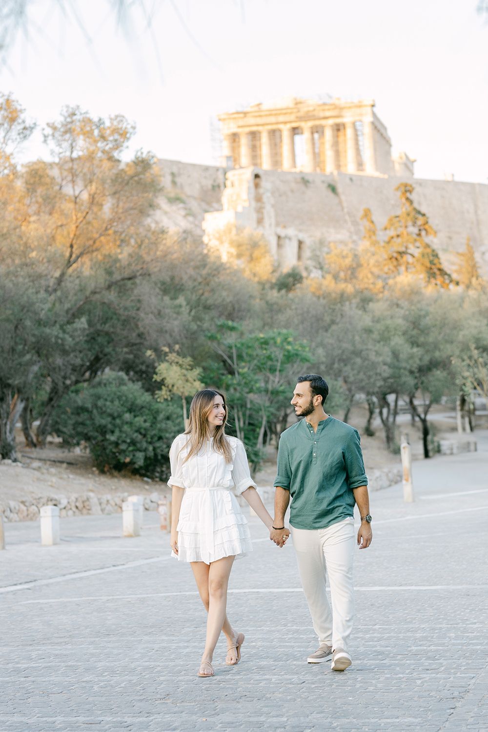Romantic couple walking playfully together near ancient ruins and stone columns during golden hour in Athens, Greece.