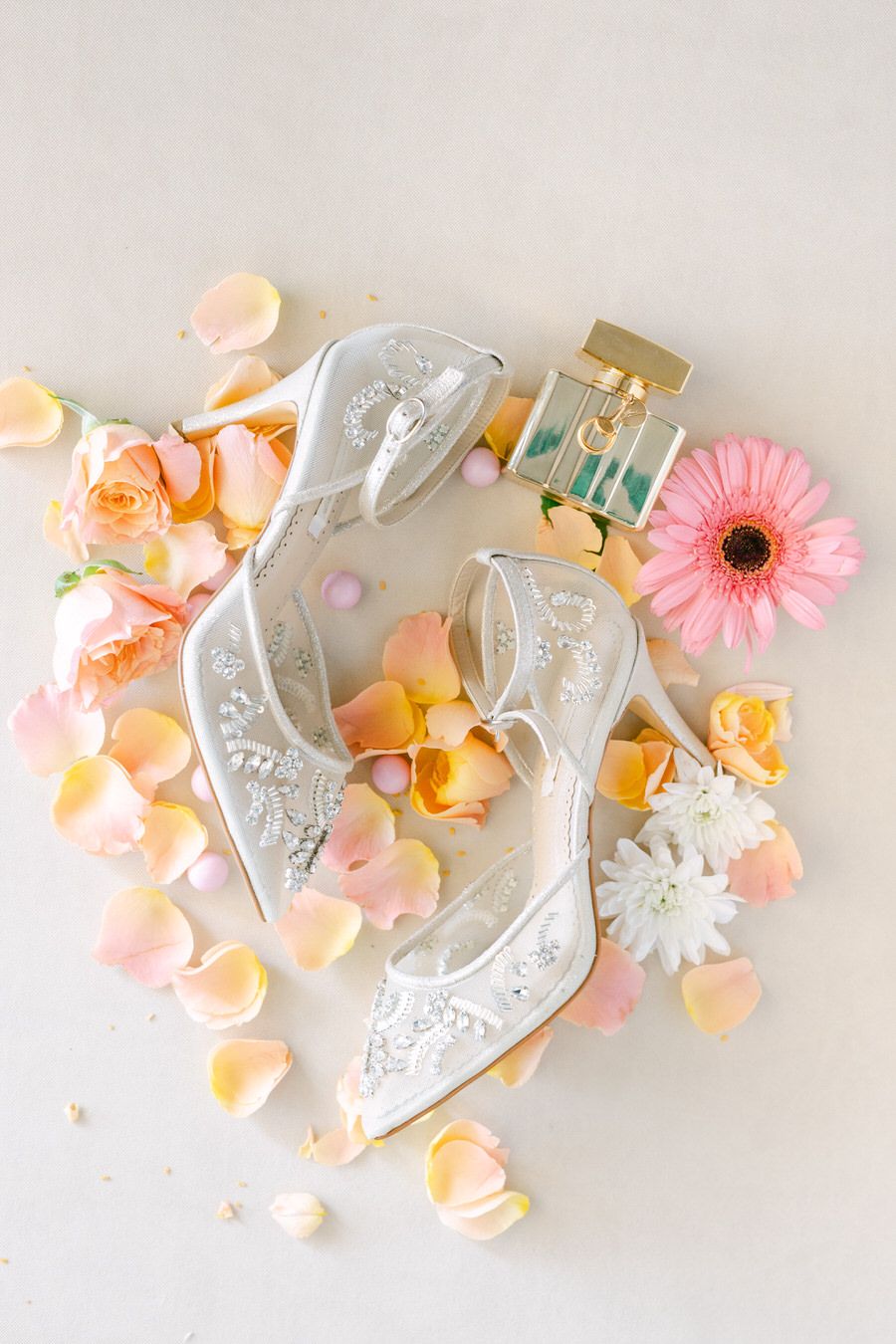 Ornate white bridal flats decorated with beading amid scattered rose petals and flowers.
