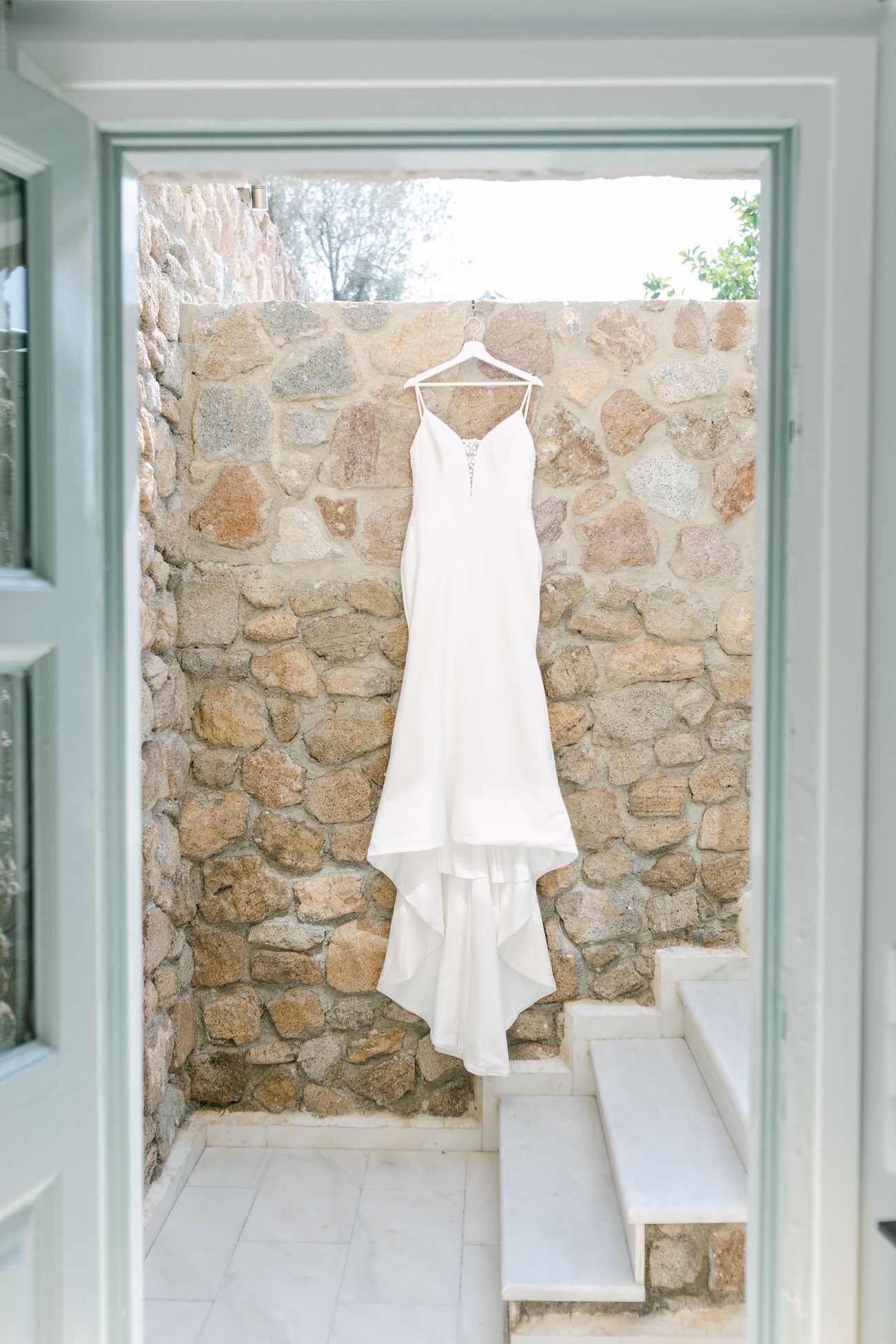 Elegant white wedding dress hanging on display against a rustic stone wall.