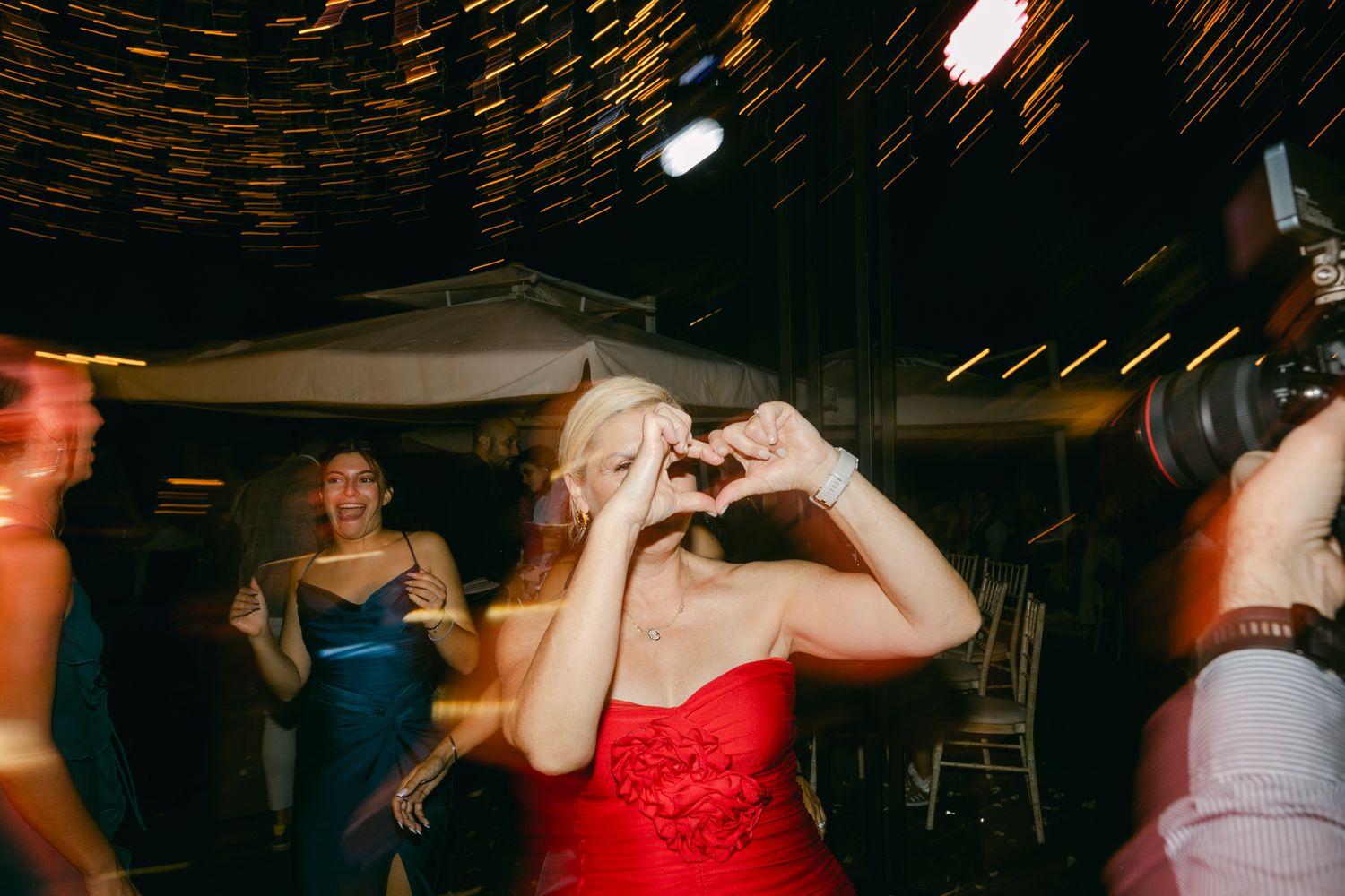 People dancing and having fun at a party with motion blur, colorful lighting and someone wearing a red dress.