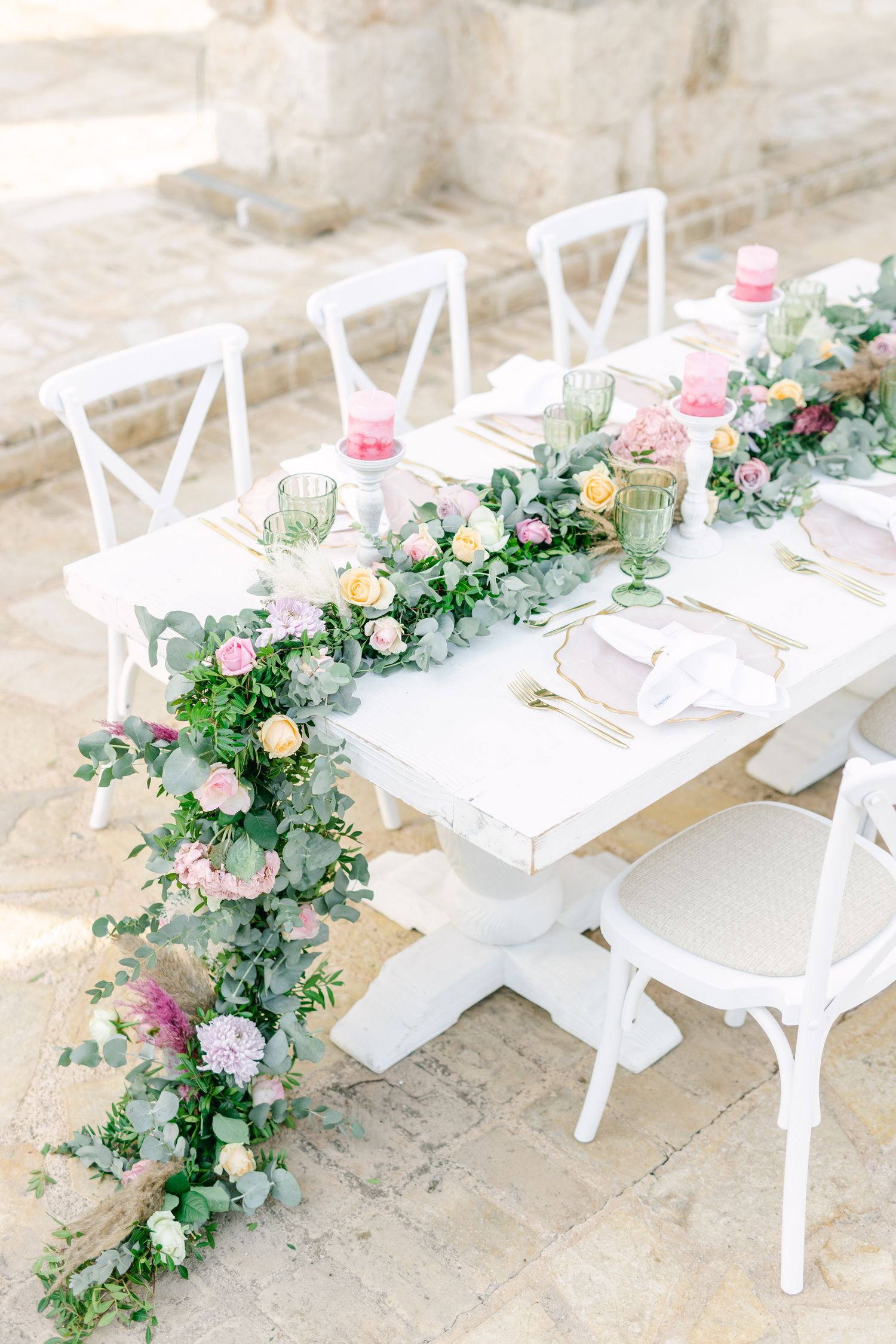 White rustic dining table decorated with lush floral garland and cross-back chairs.