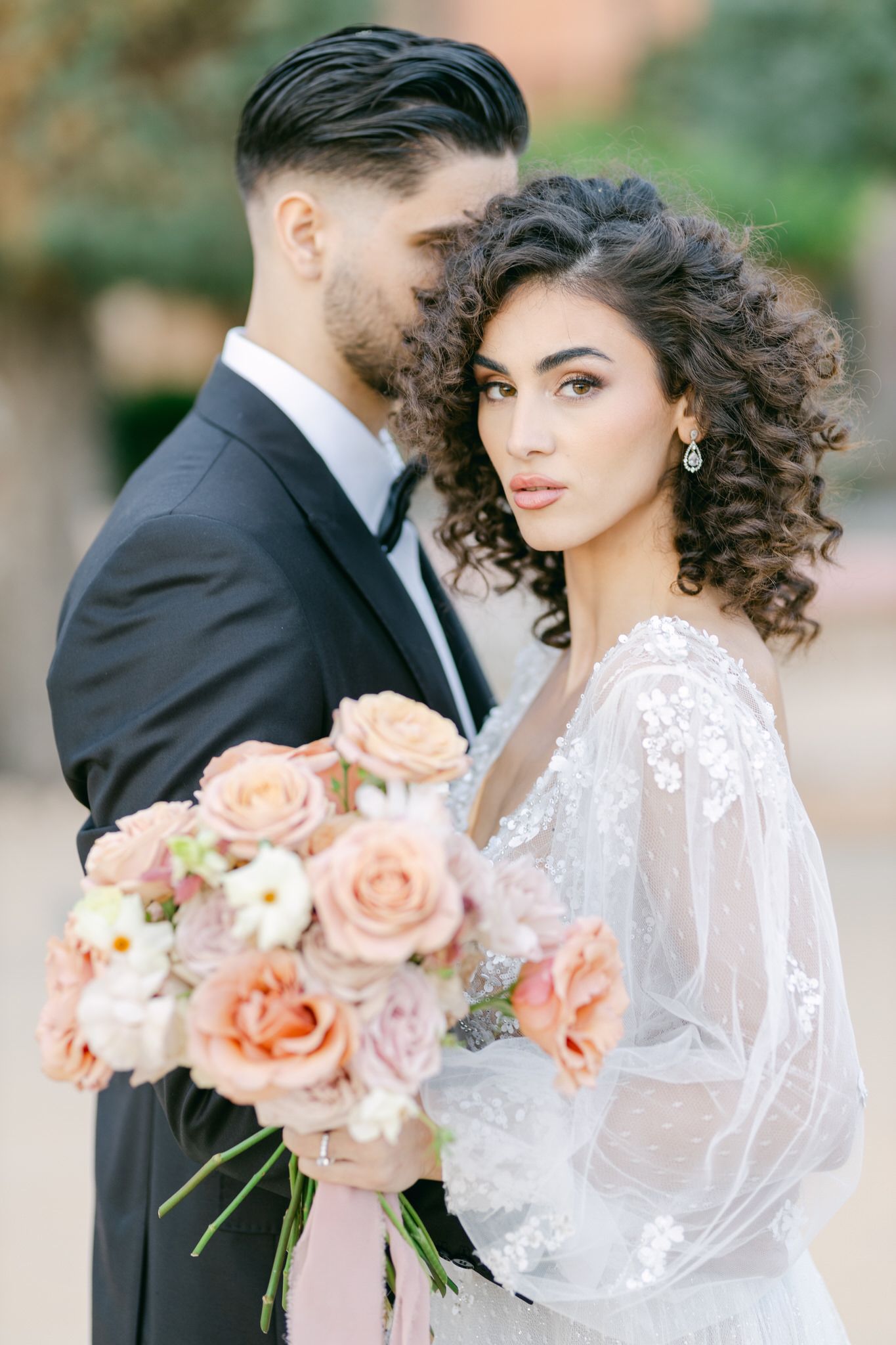 Romantic wedding portrait with peach roses and white lace gown against soft blurred background.