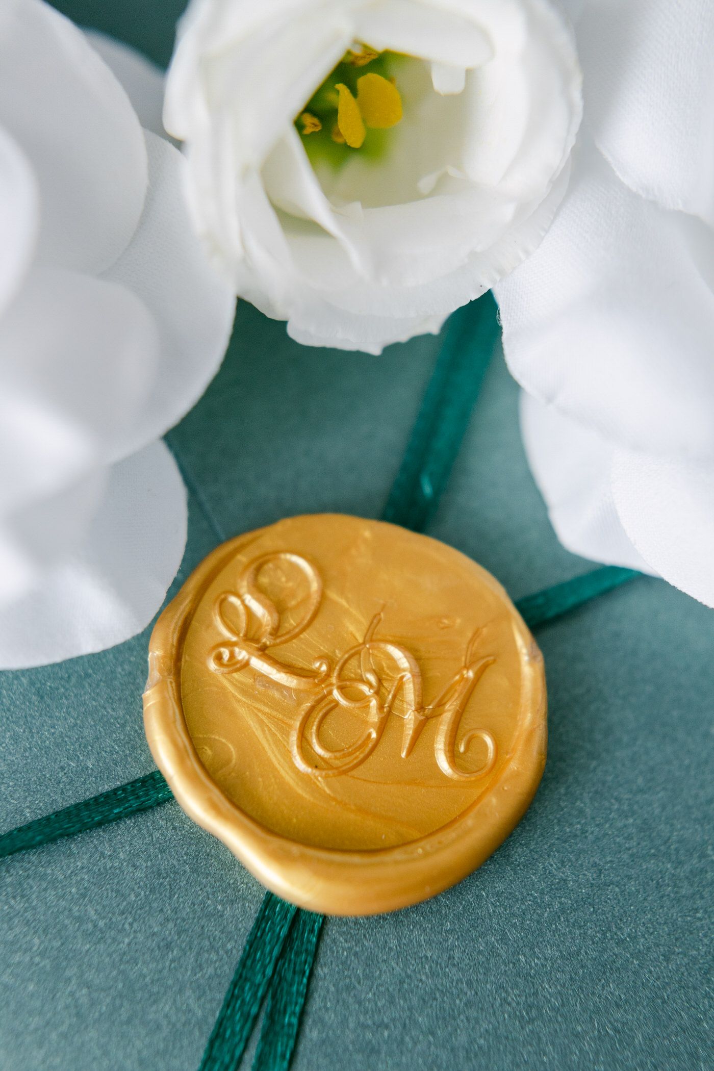 Gold wax seal with monogram on emerald green envelope with white flowers.