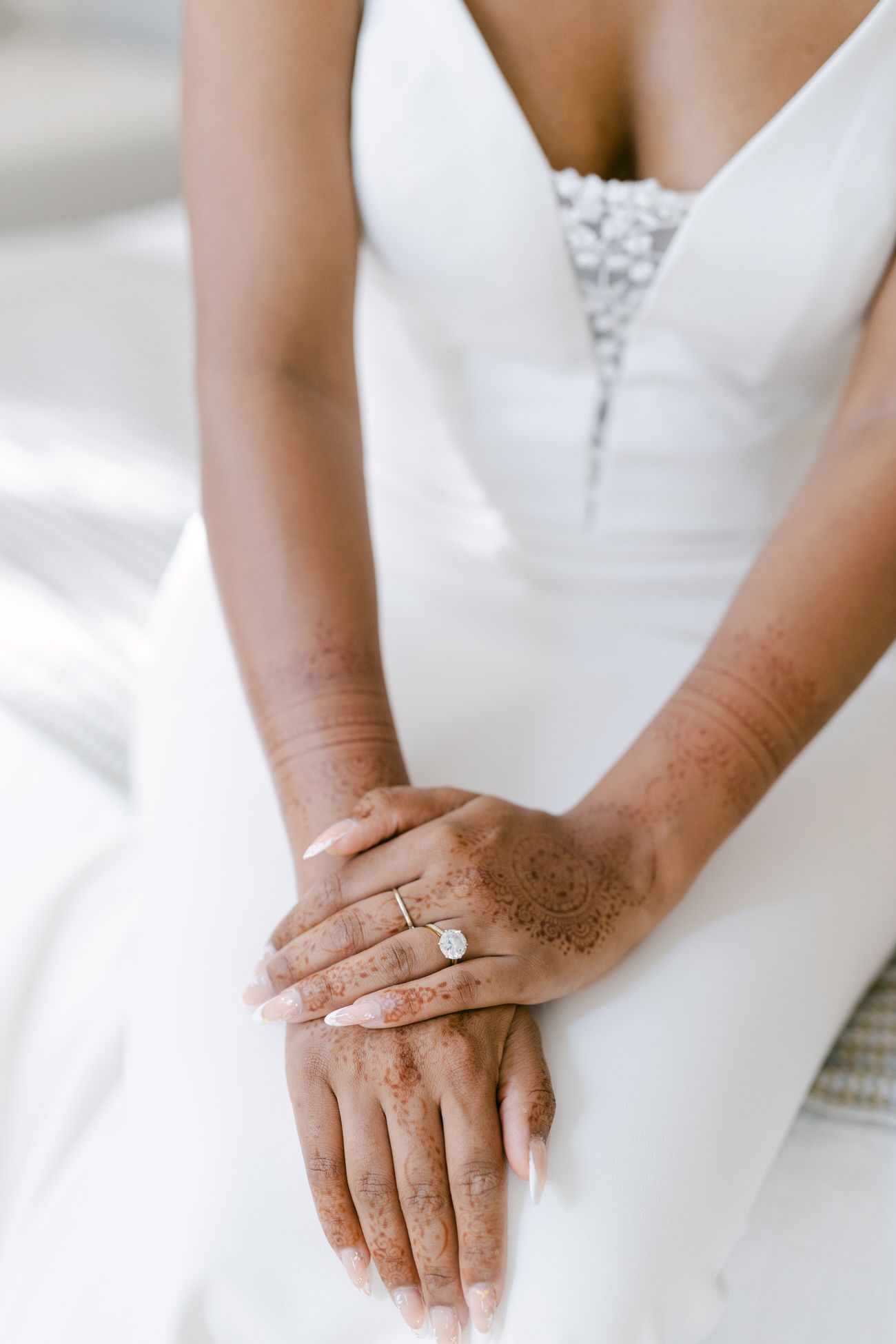 Close up of hands with engagement ring resting on white wedding dress fabric.