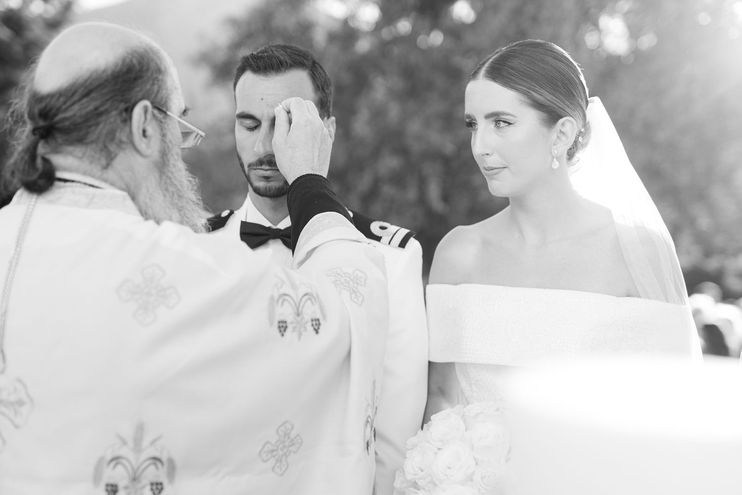 A black and white photo captures a traditional wedding ceremony being performed by a priest outdoors.