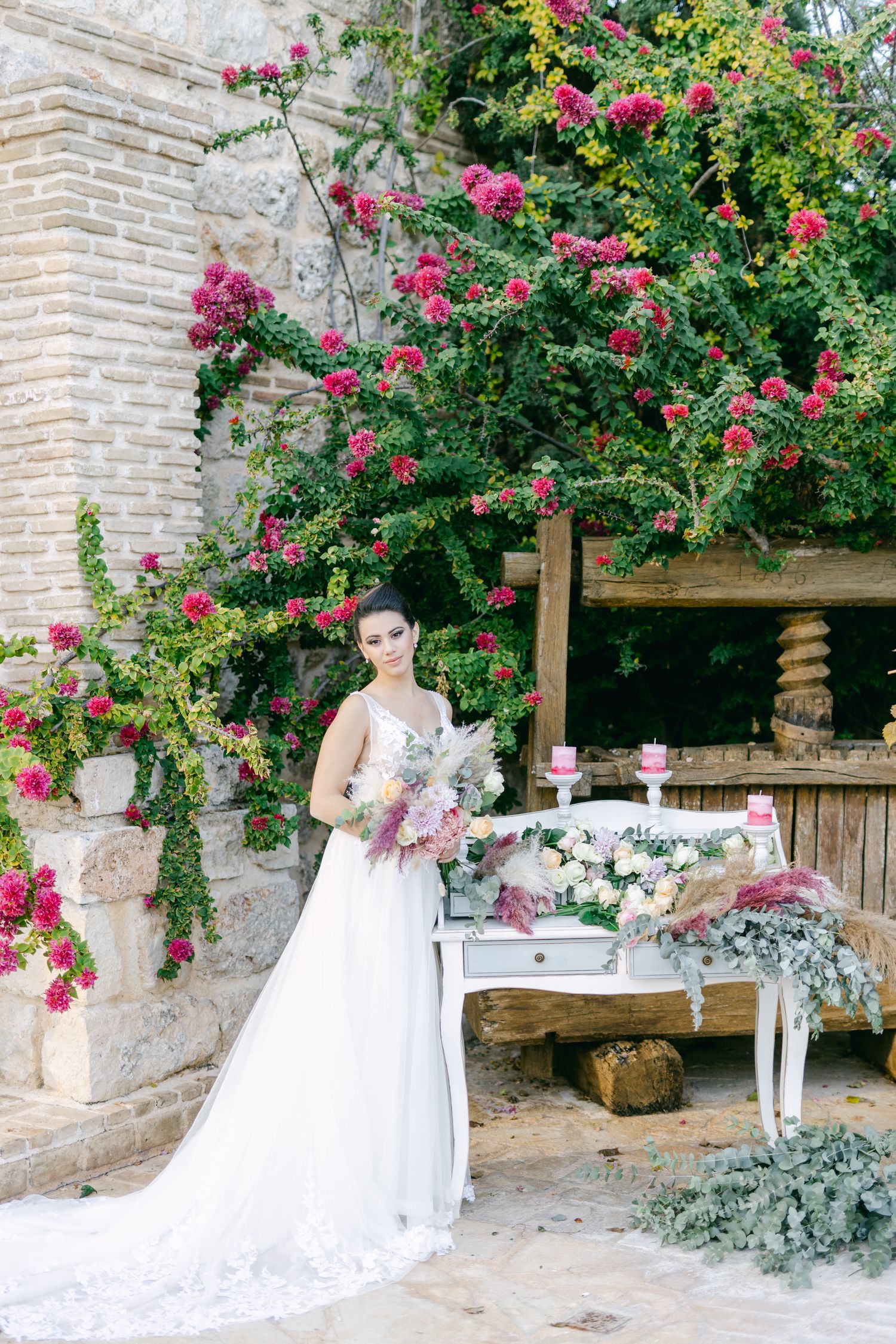 Elegant wedding scene with a white table and climbing pink roses against a stone wall.
