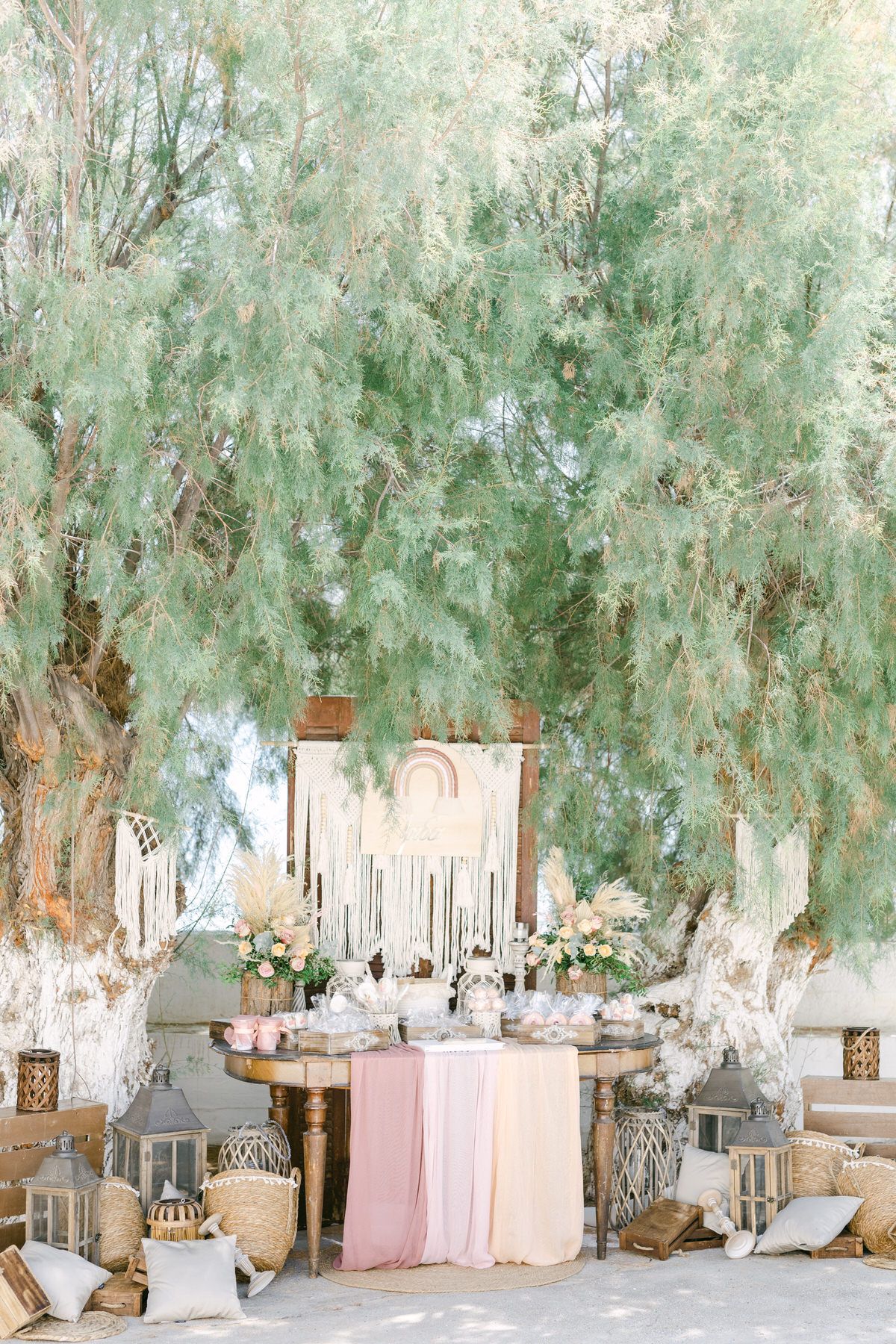 Elegant outdoor wedding decor setup with vintage furniture, blush draping and floral arrangements under whimsical willow trees.