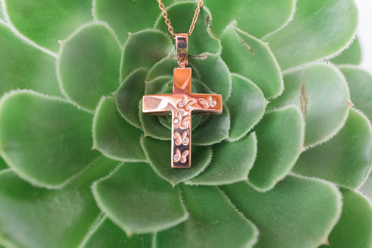 A copper cross pendant with floral design rests on green succulent leaves.