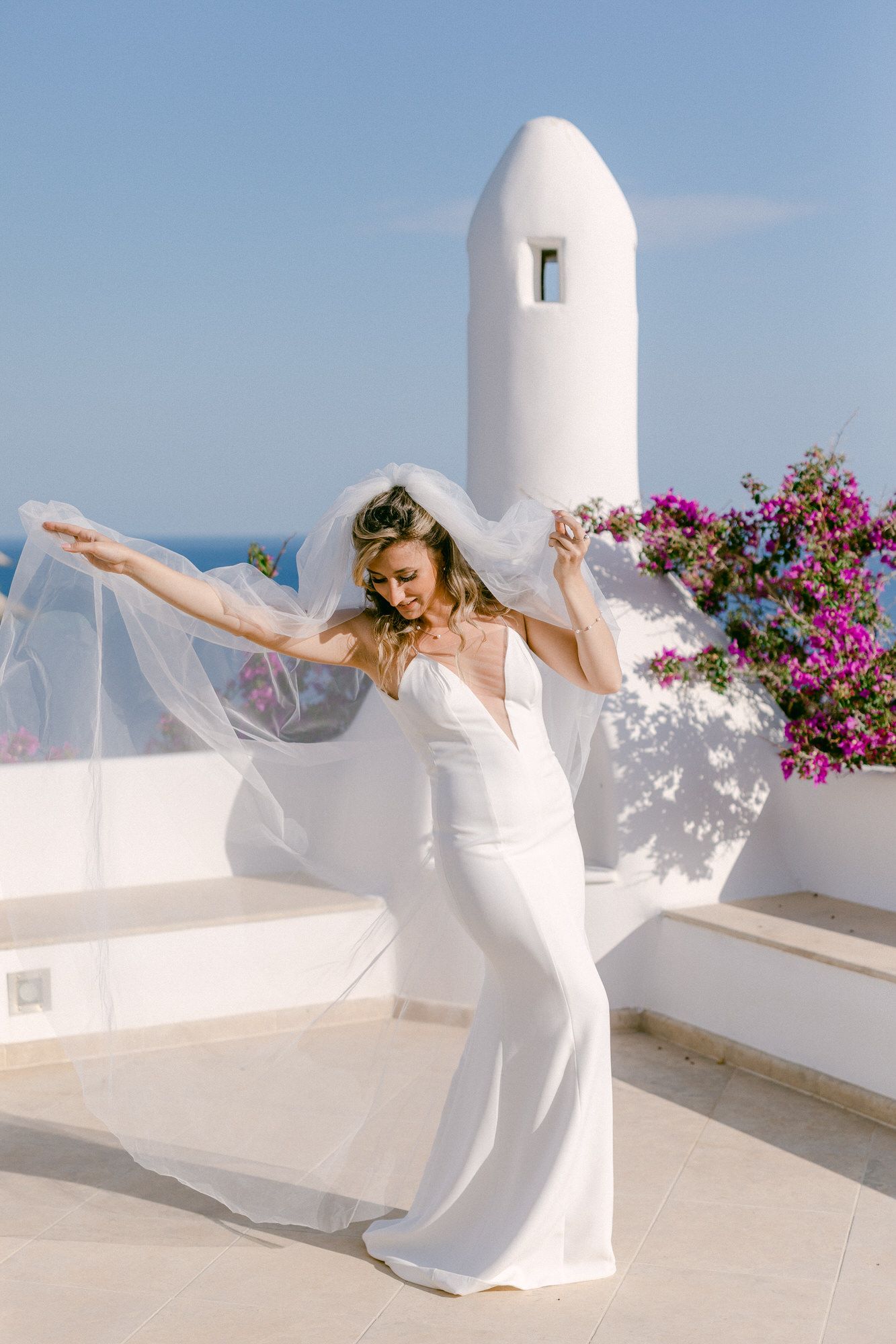 Flowing white wedding dress against Mediterranean architecture with bougainvillea flowers.
