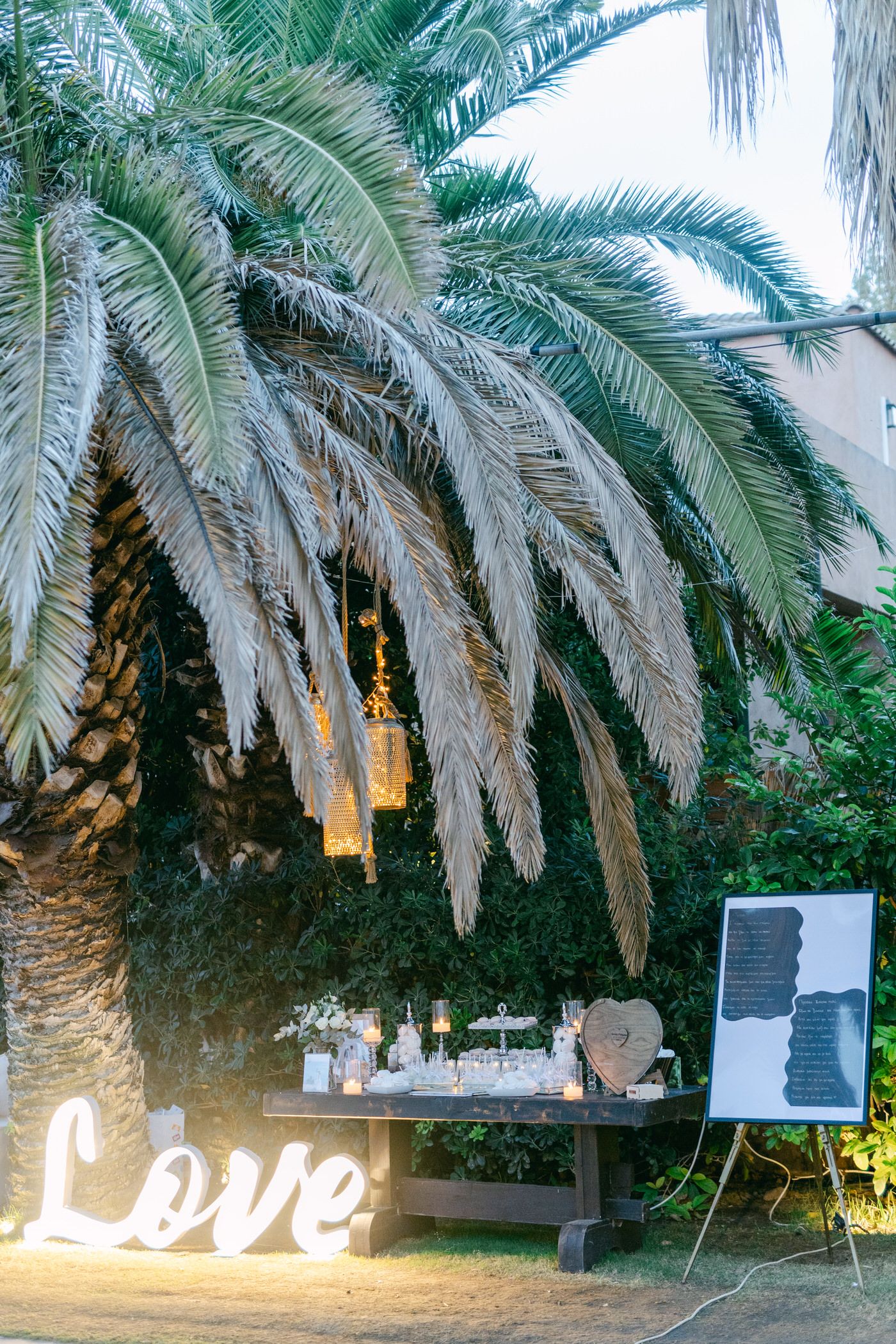 Palm tree illuminated at dusk with glowing 'Love' sign and event decor beneath fronds.