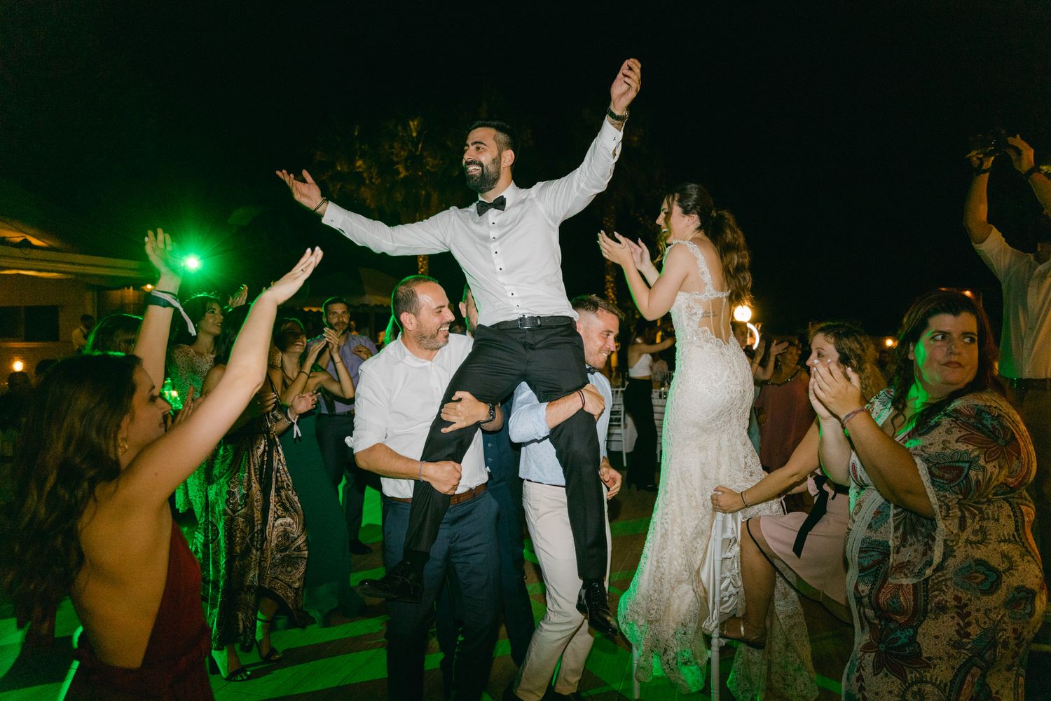 Wedding reception party guests lift someone up on the dance floor during an energetic celebration at night.