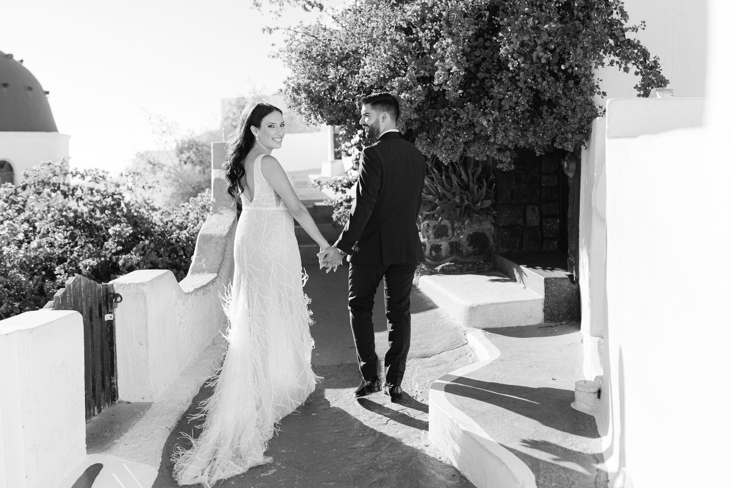Newlywed couple walking up white stairs on wedding day in black and white photography.