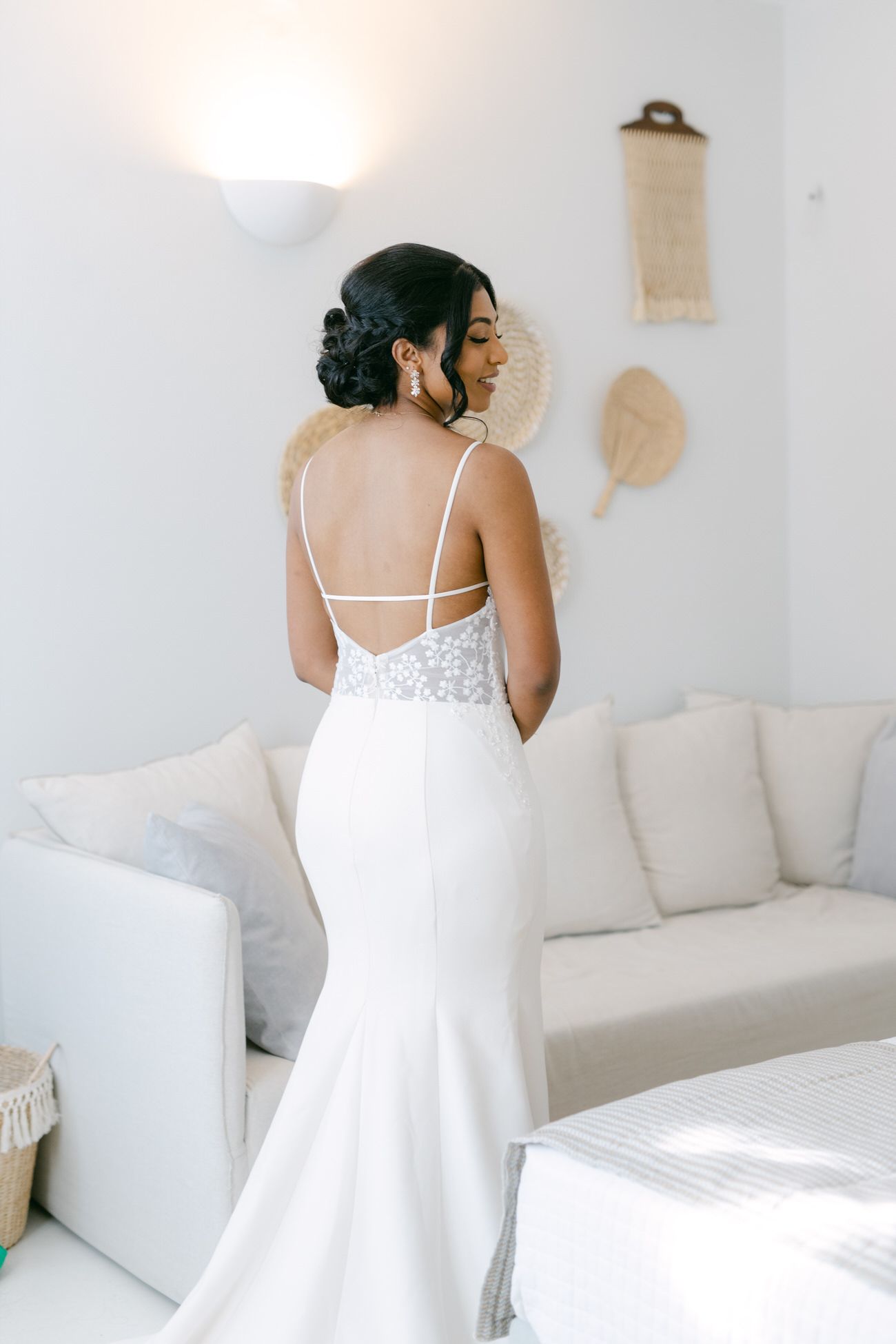 Back view of bride in fitted white lace dress against white interior decor.