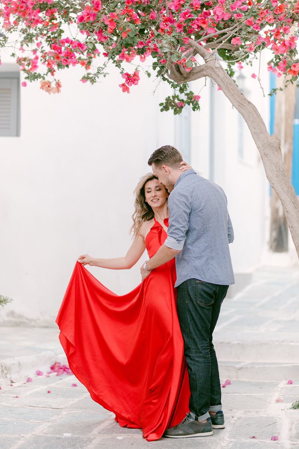 A romantic moment under pink bougainvillea flowers in a white-walled Mediterranean setting.