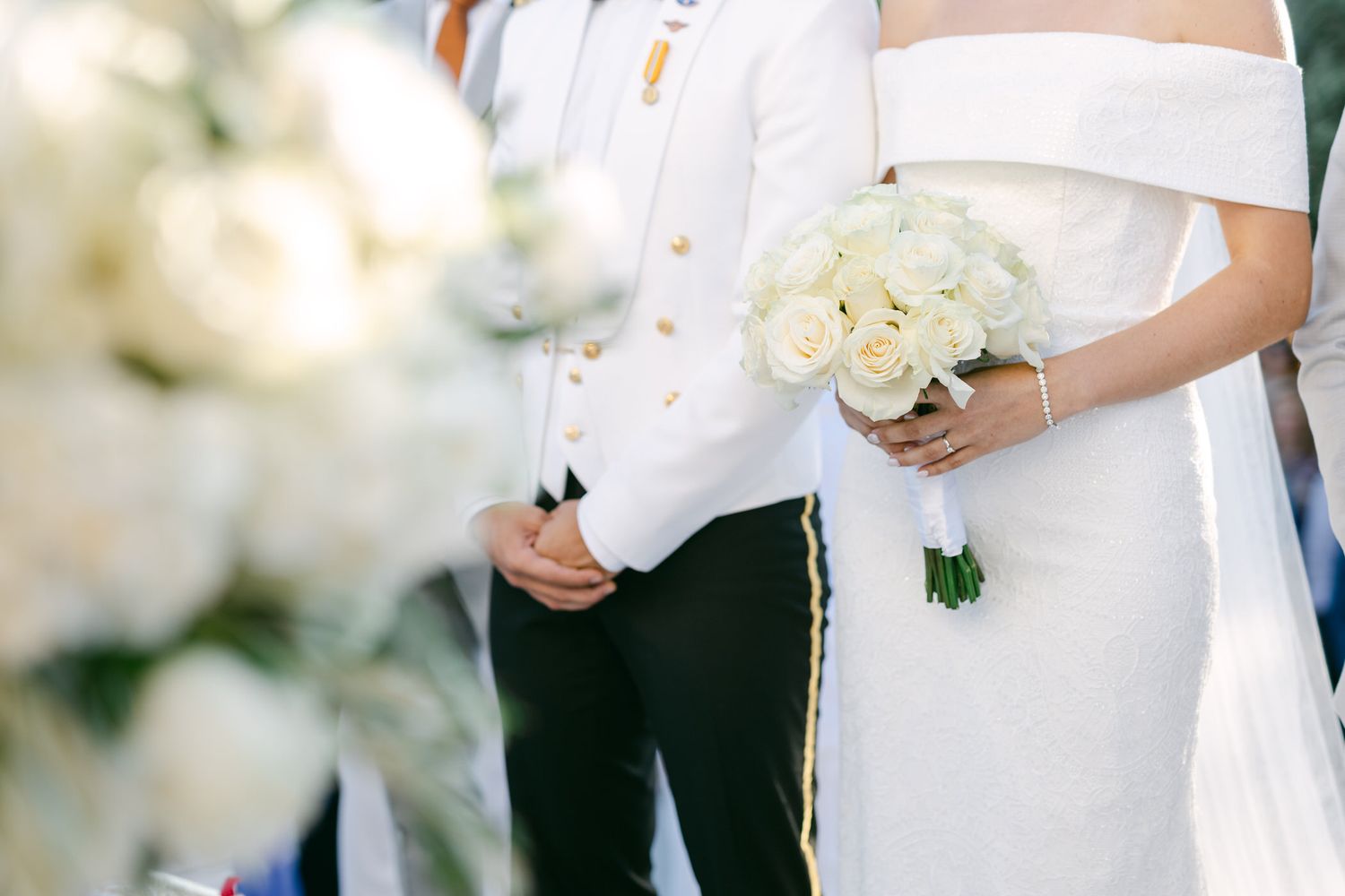Wedding ceremony close-up showing couple holding champagne glass and white bouquet in elegant attire.