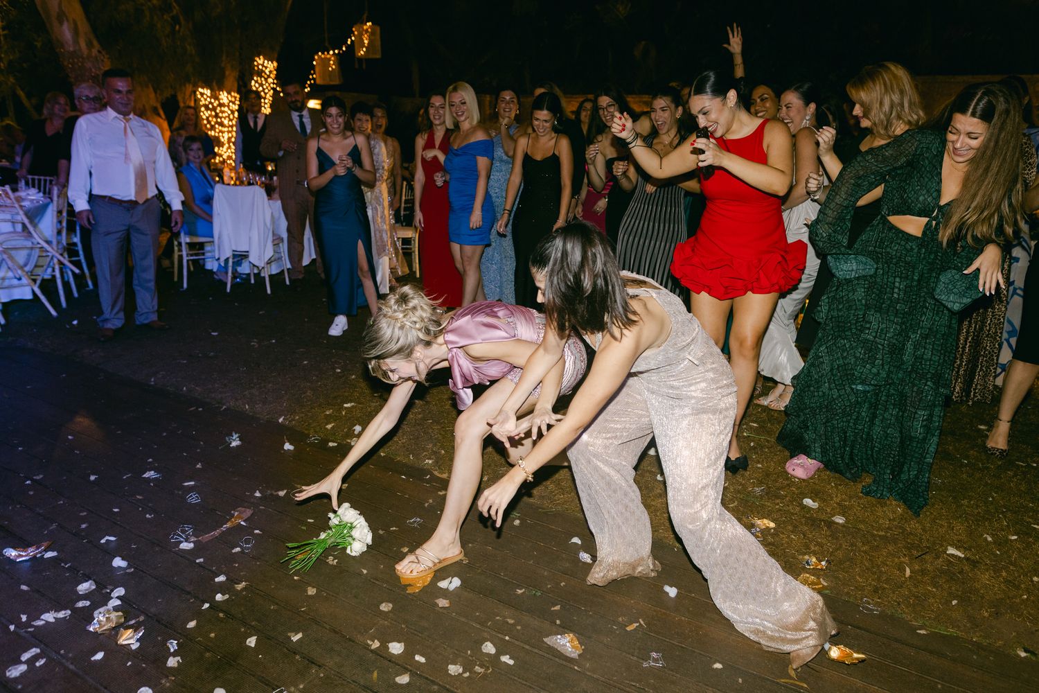Party guests bend down to collect items from the dance floor while others dance at a nighttime celebration.