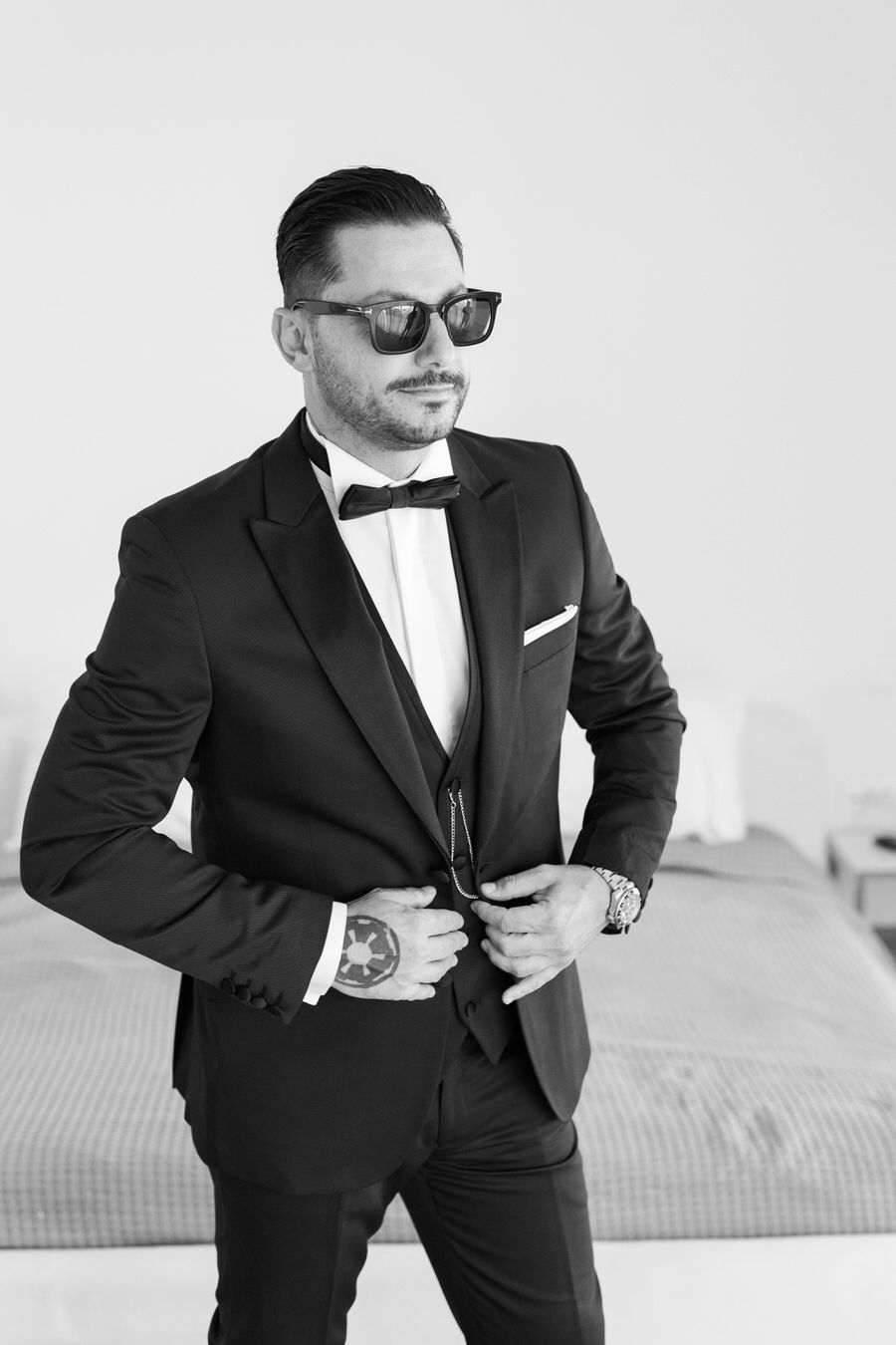 Groom adjusting jacket in sophisticated black and white portrait.