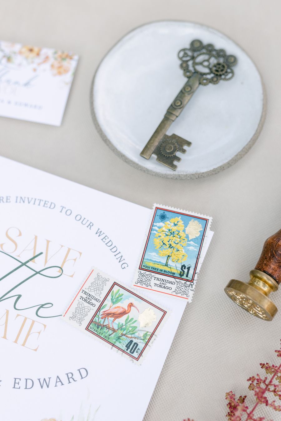 Vintage decorative key on white plate next to wedding invitation and postage stamps.