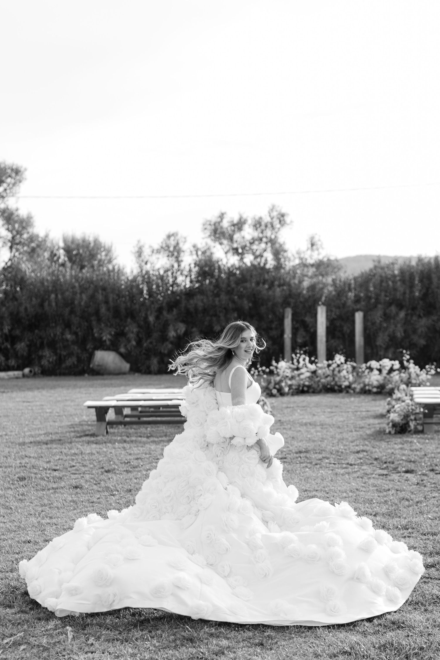 Black and white photo of a bride in a flowing white ballgown dress twirling on a garden lawn at sunset.