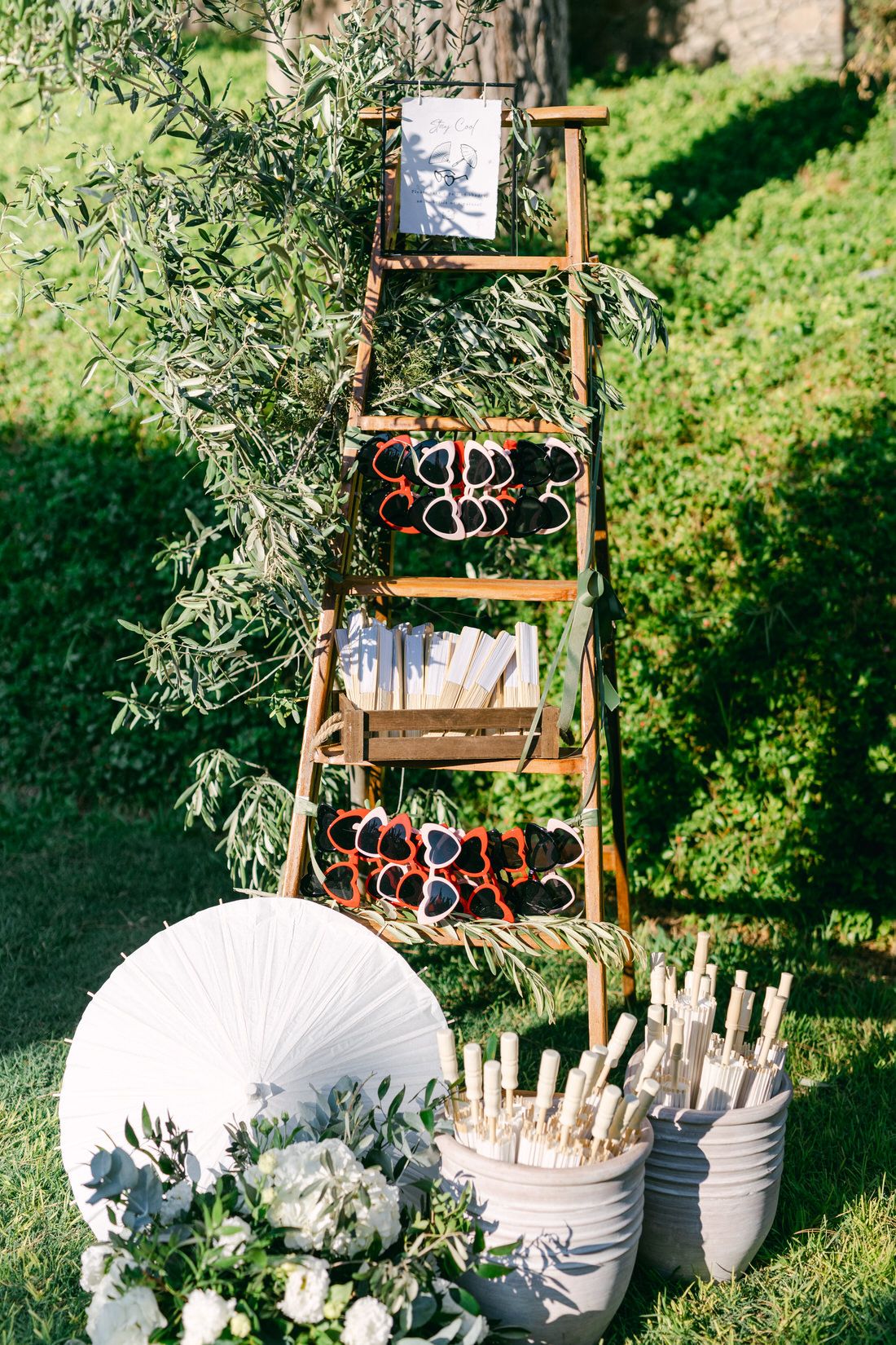 A decorative wooden ladder display with parasols and floral arrangements on a grassy lawn for a garden wedding setup.