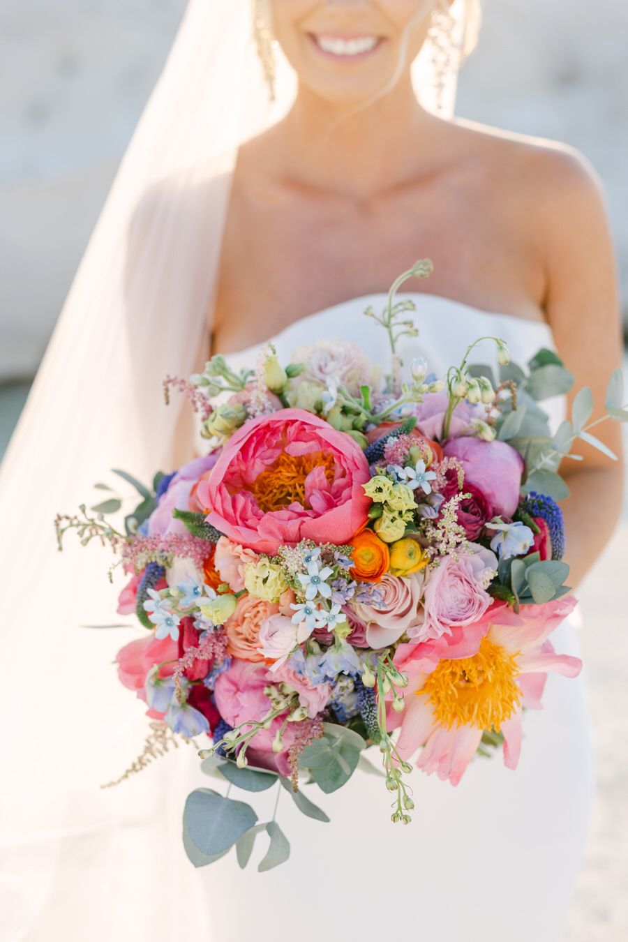Vibrant pink and coral garden-style bridal bouquet with garden roses, eucalyptus and wildflowers in sunlit wedding photo.