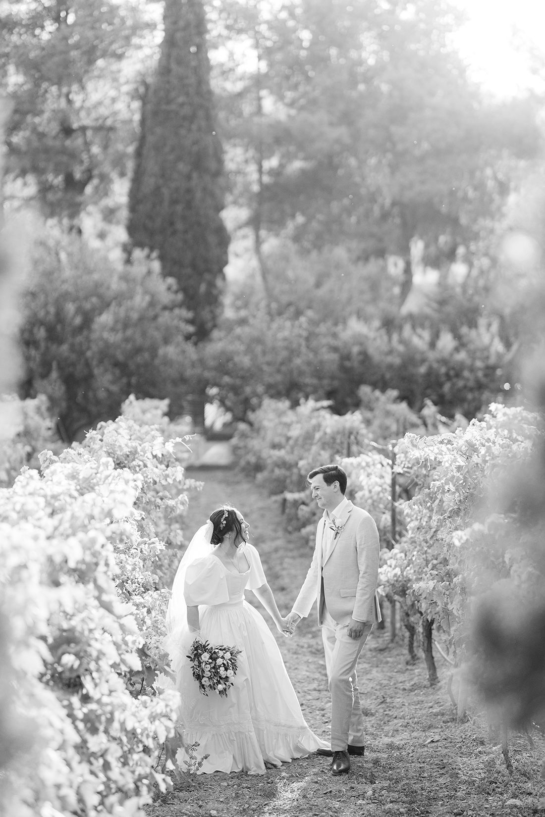A romantic wedding scene shows a couple walking together between rows of flowers on a misty garden path.