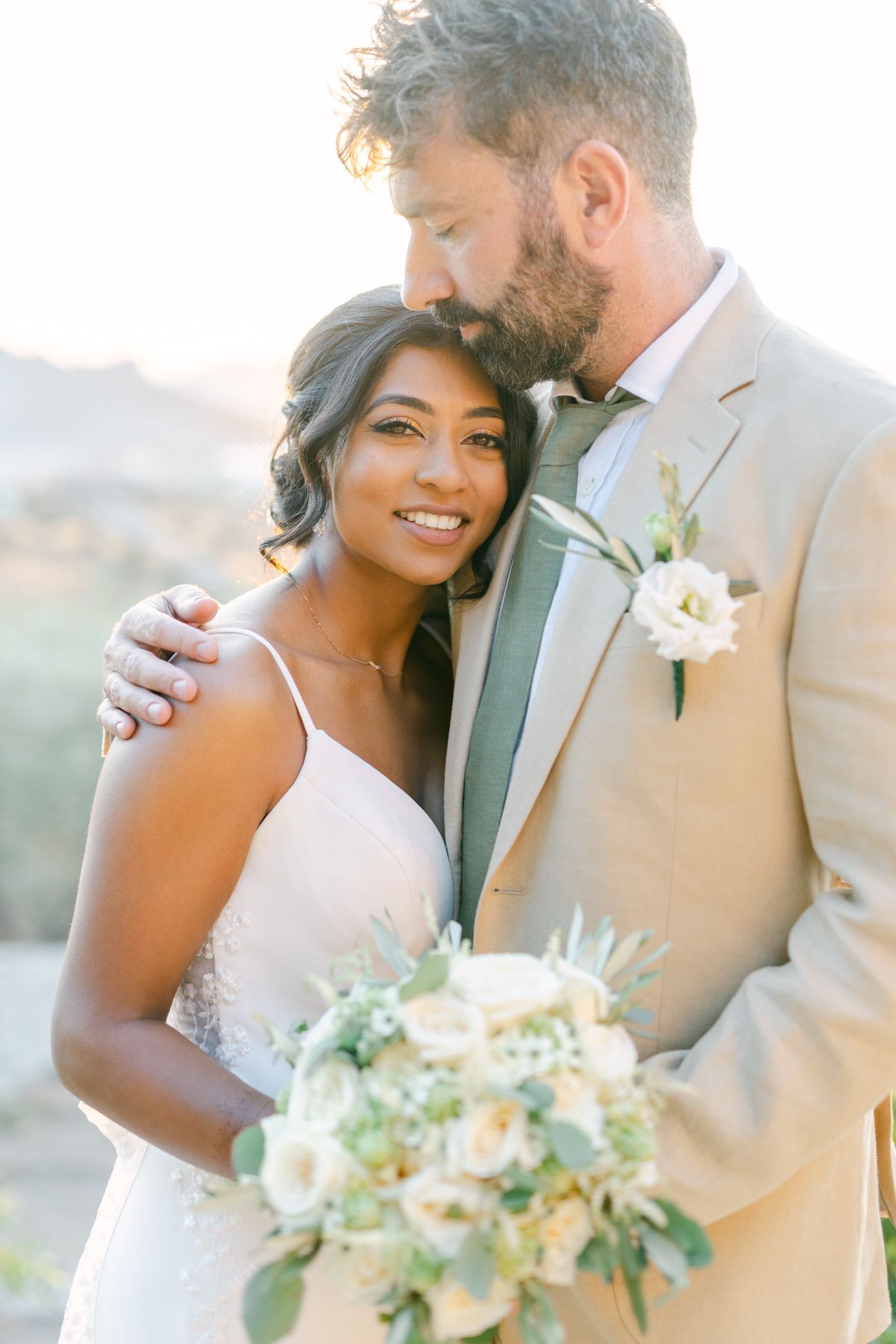 A tender moment between newlyweds in formal attire with a beautiful mountain backdrop at sunset.