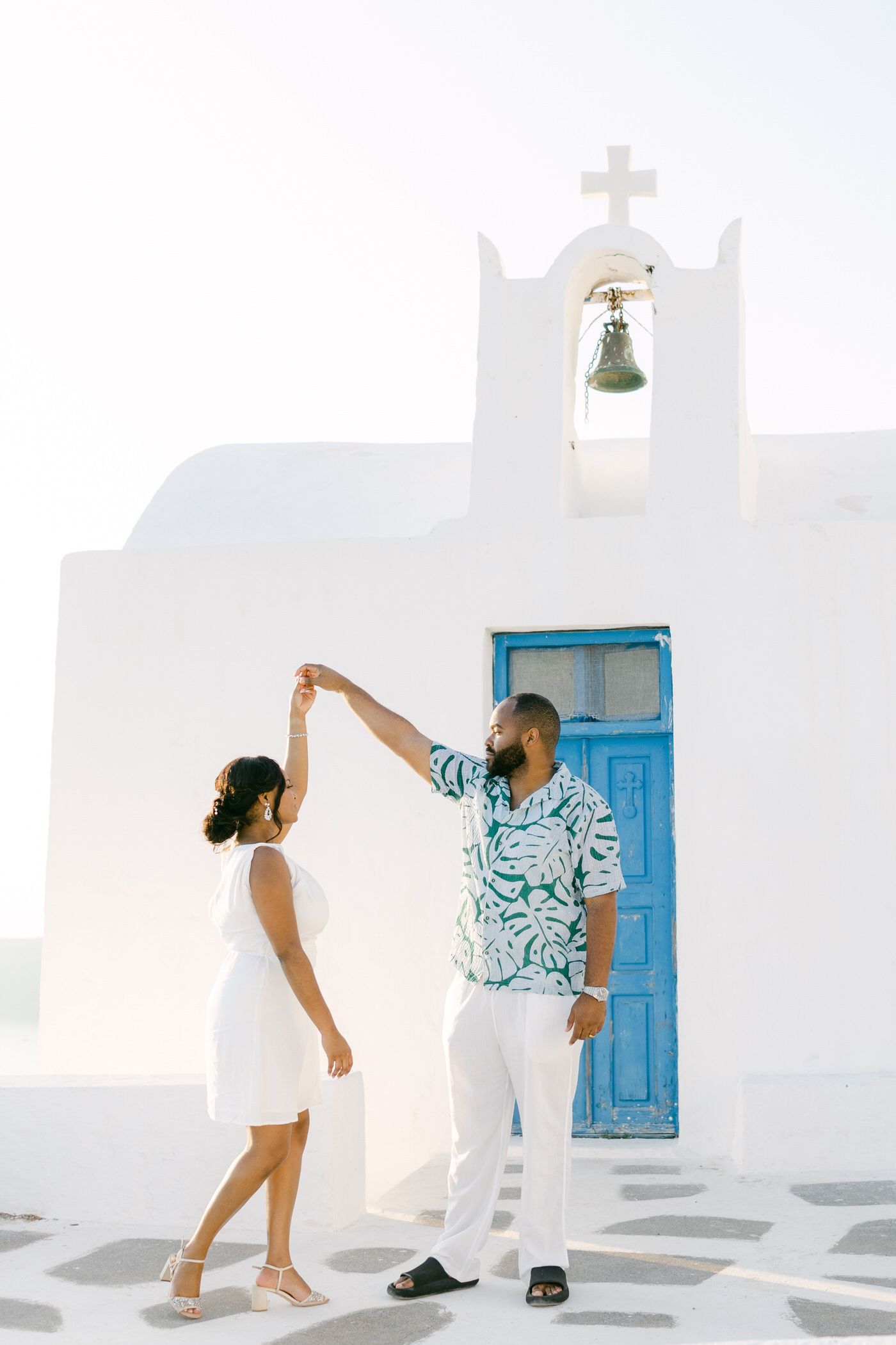 A bride and groom wearing sunglasses walk together holding champagne and flowers in a white stairwell.