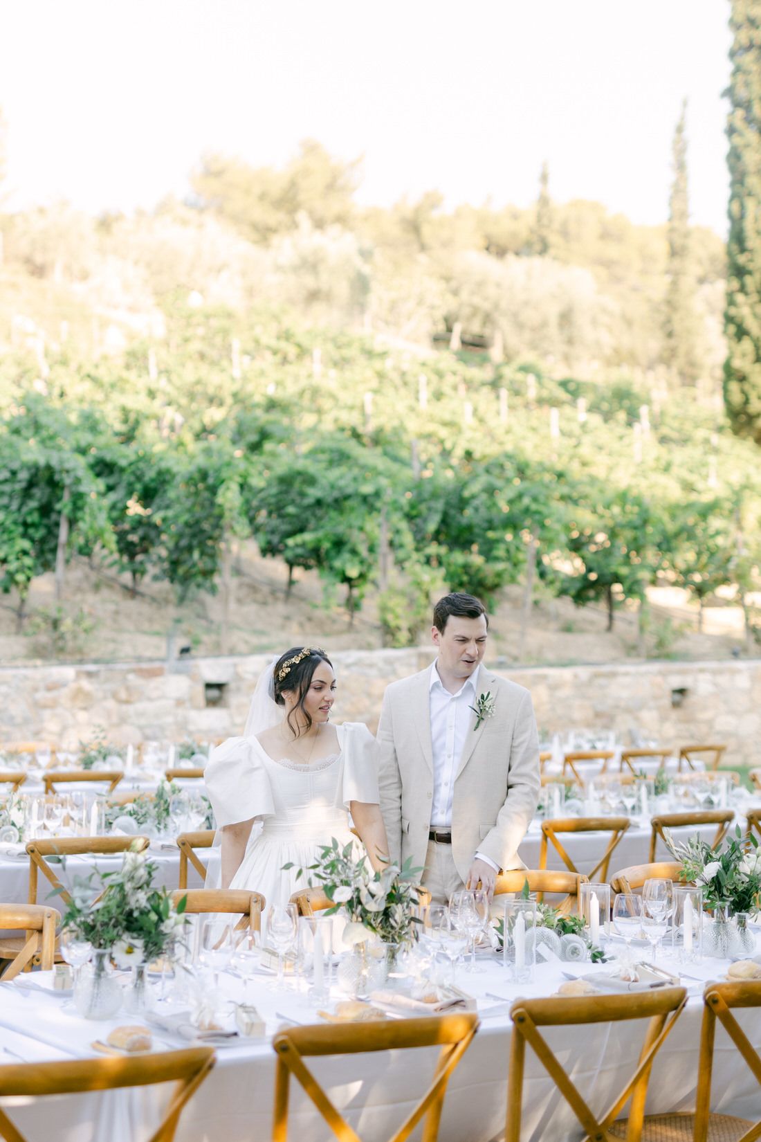 An outdoor wedding reception table setup with wooden chairs and elegant place settings in a garden vineyard setting.