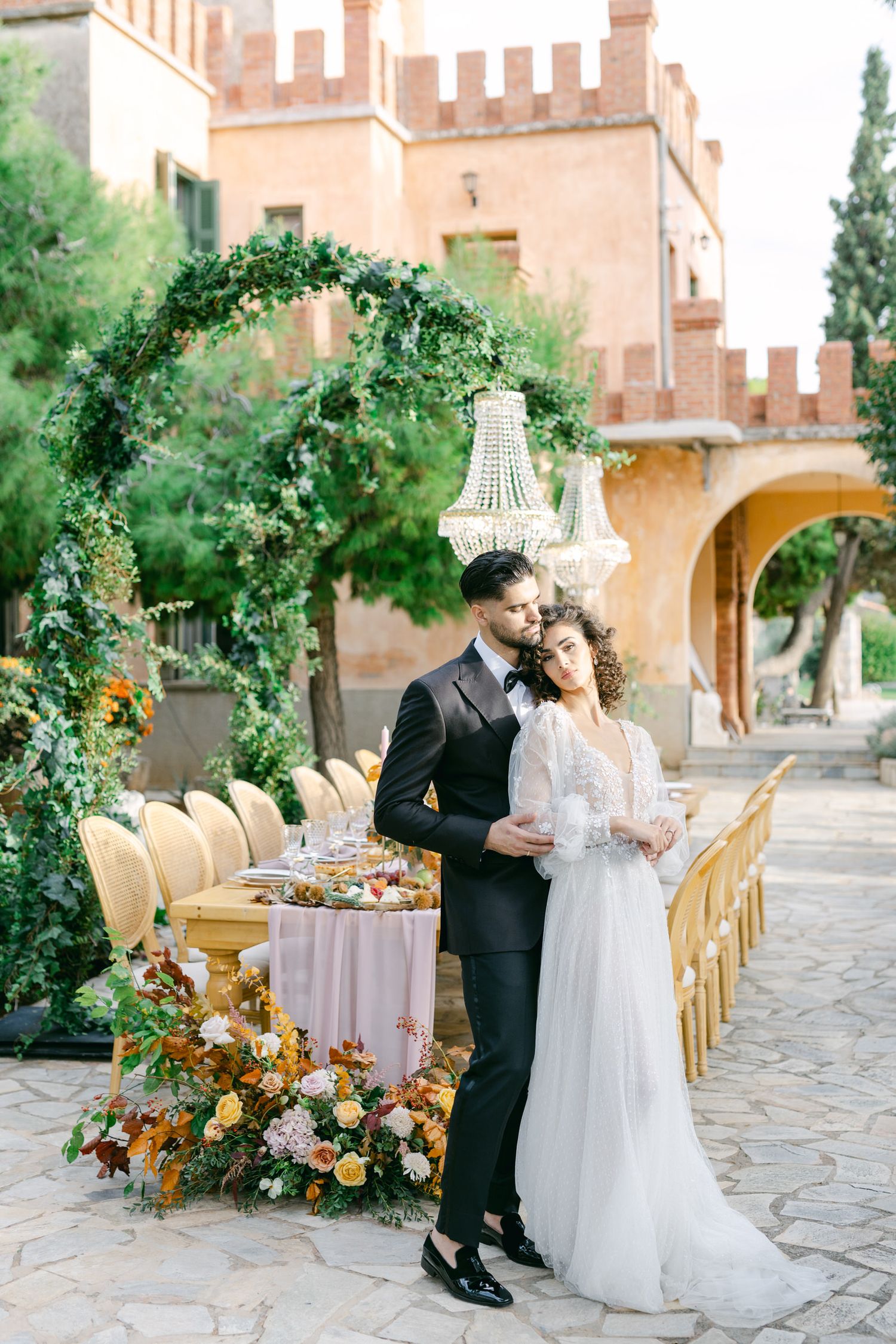 Elegant outdoor wedding reception setup with floral arch, chandelier and dining table against Pyrgos Melissourgou